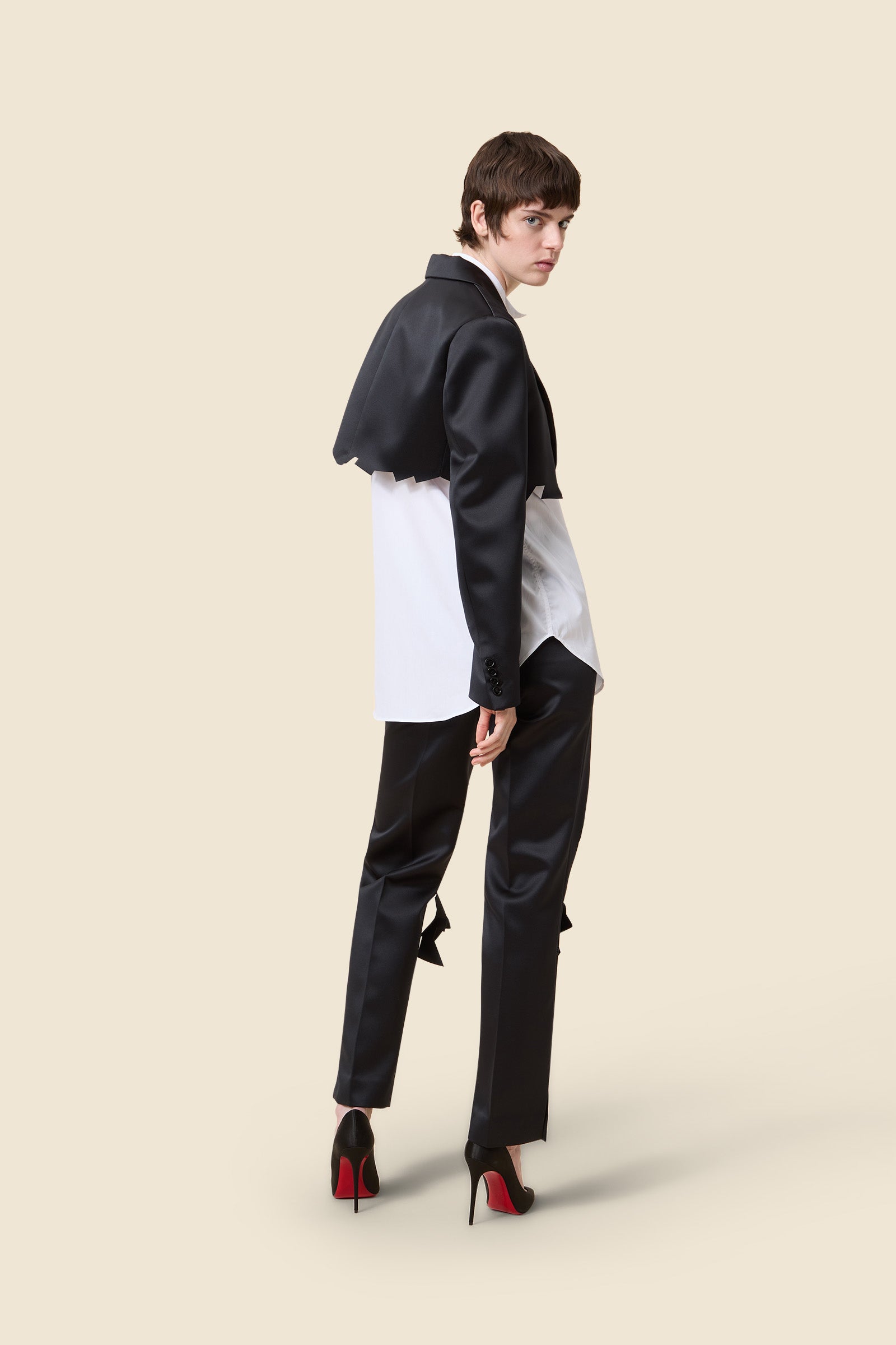 Model wearing a cream sweater with sheer zigzag design and sleek black straight-leg trousers on a plain background.