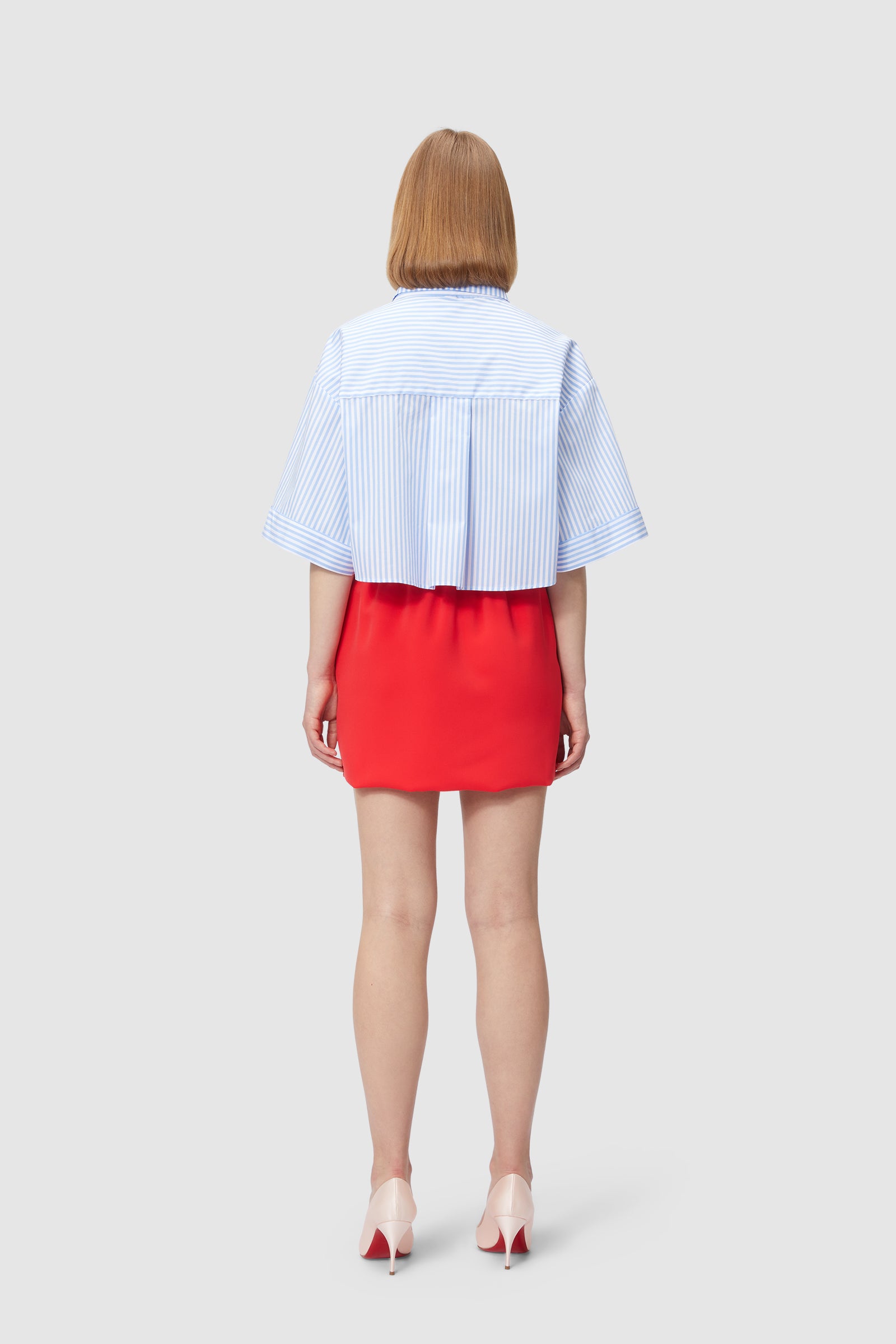 A blue pinstripe shirt with wide sleeves paired with a vibrant red mini skirt and cream high heels, viewed from the back.
