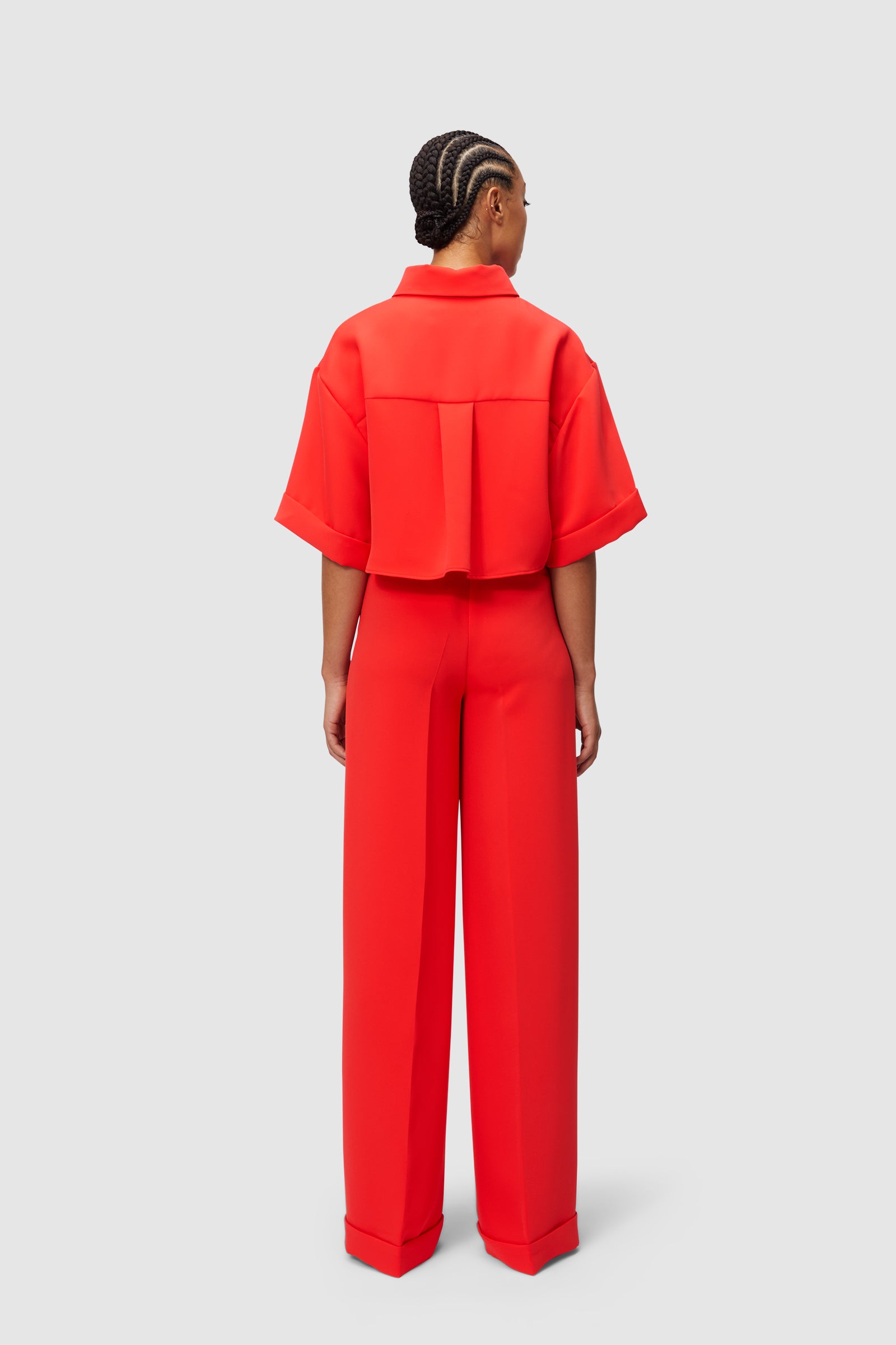 Red ensemble featuring a structured short-sleeve shirt with box pleats and high-waisted wide-leg trousers.