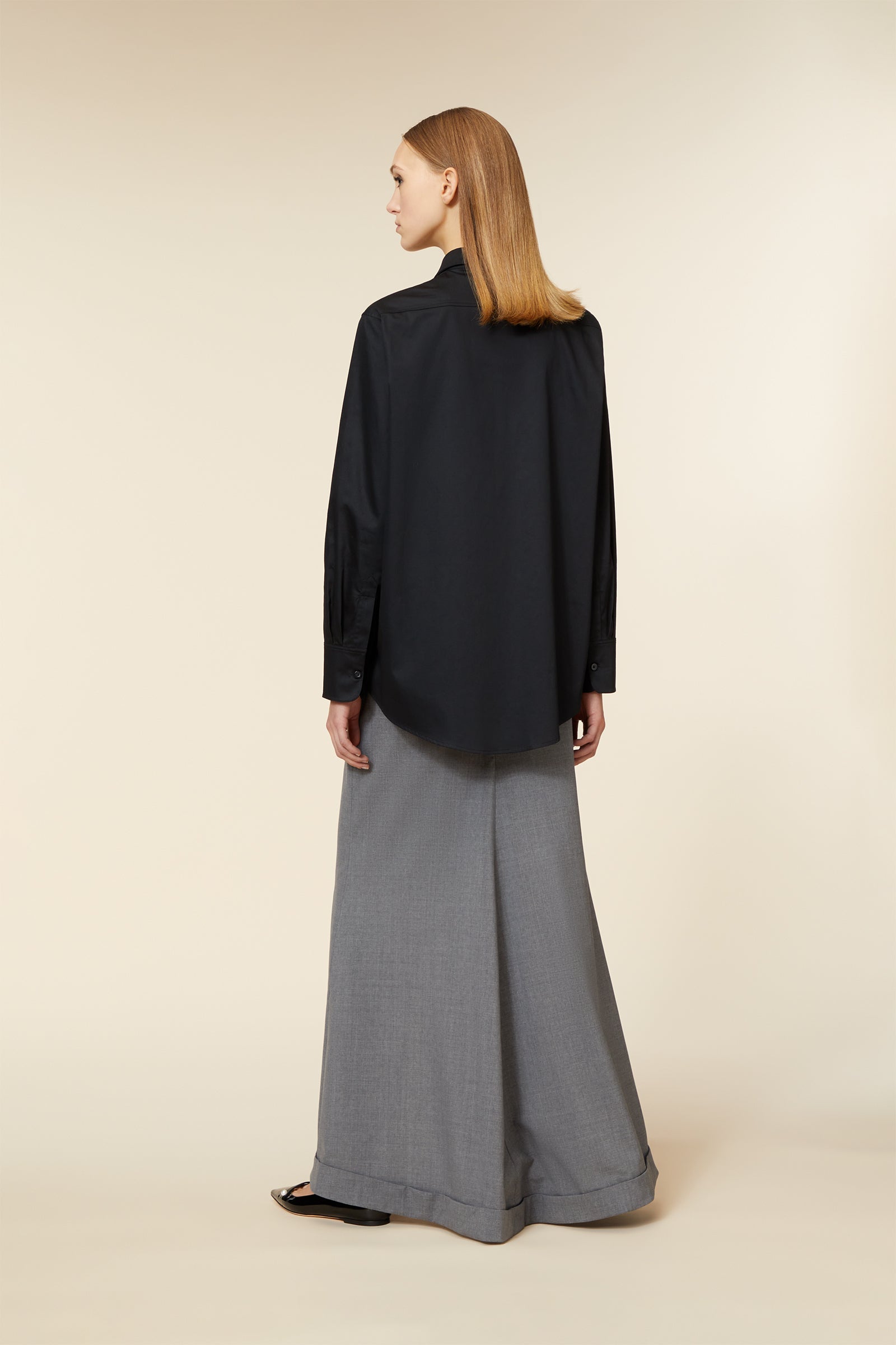 A tailored black blouse with an elegant draped hem gracefully paired with sophisticated wide-leg gray trousers.
