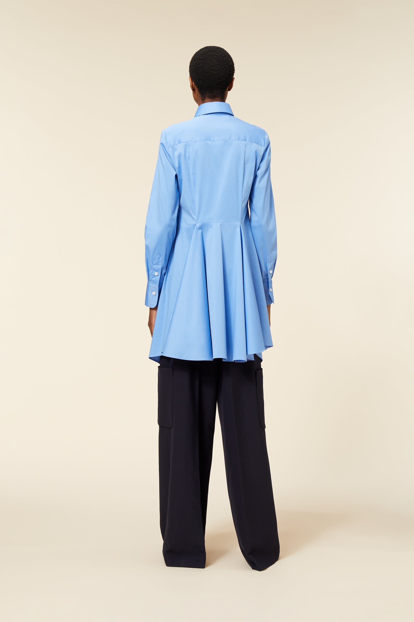 Light blue button-down shirt with a flared, pleated hem, paired with wide-leg, black cargo trousers from the back view.