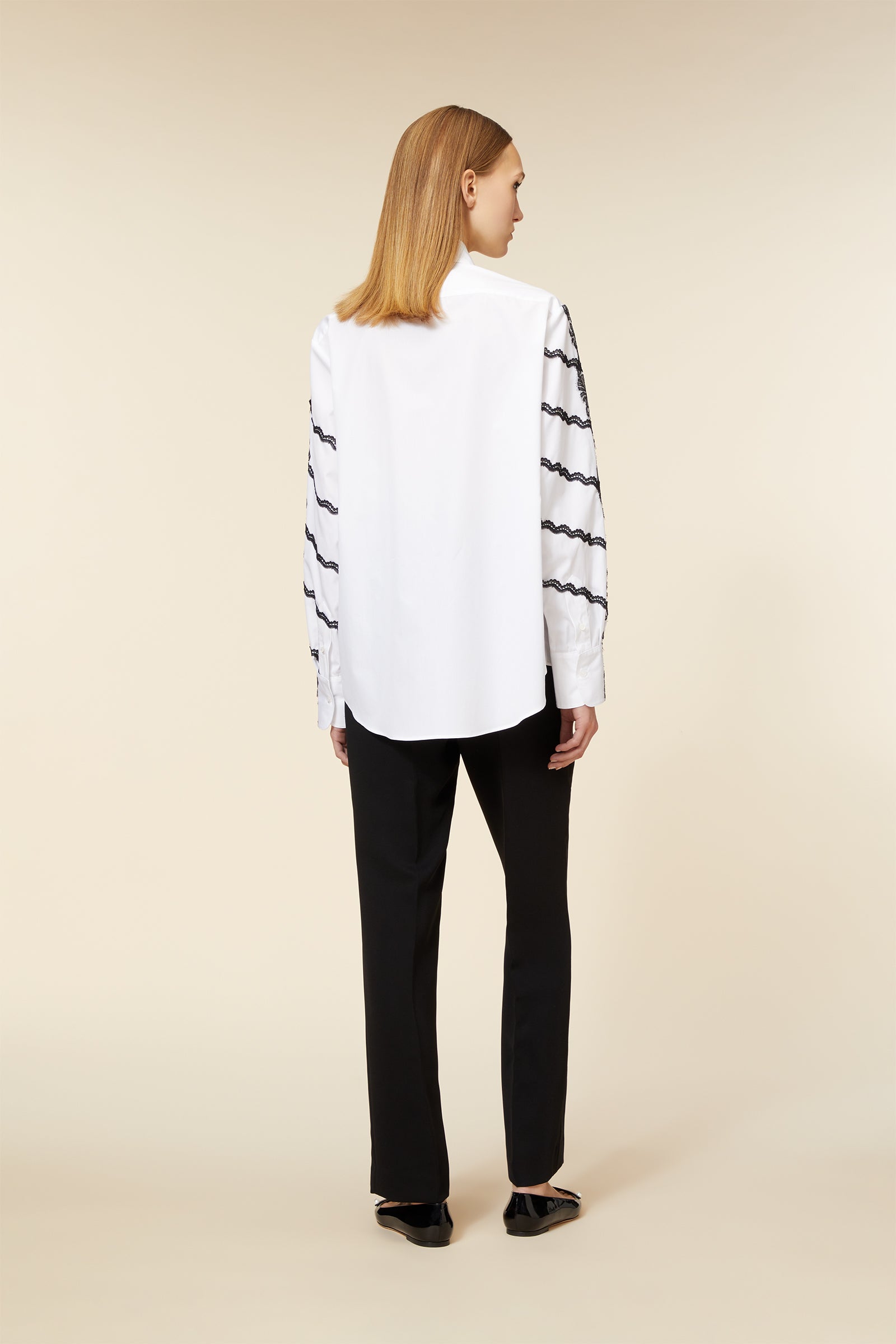 White button-up shirt with black wave-patterned sleeves, paired with sleek black trousers, styled with black patent loafers.