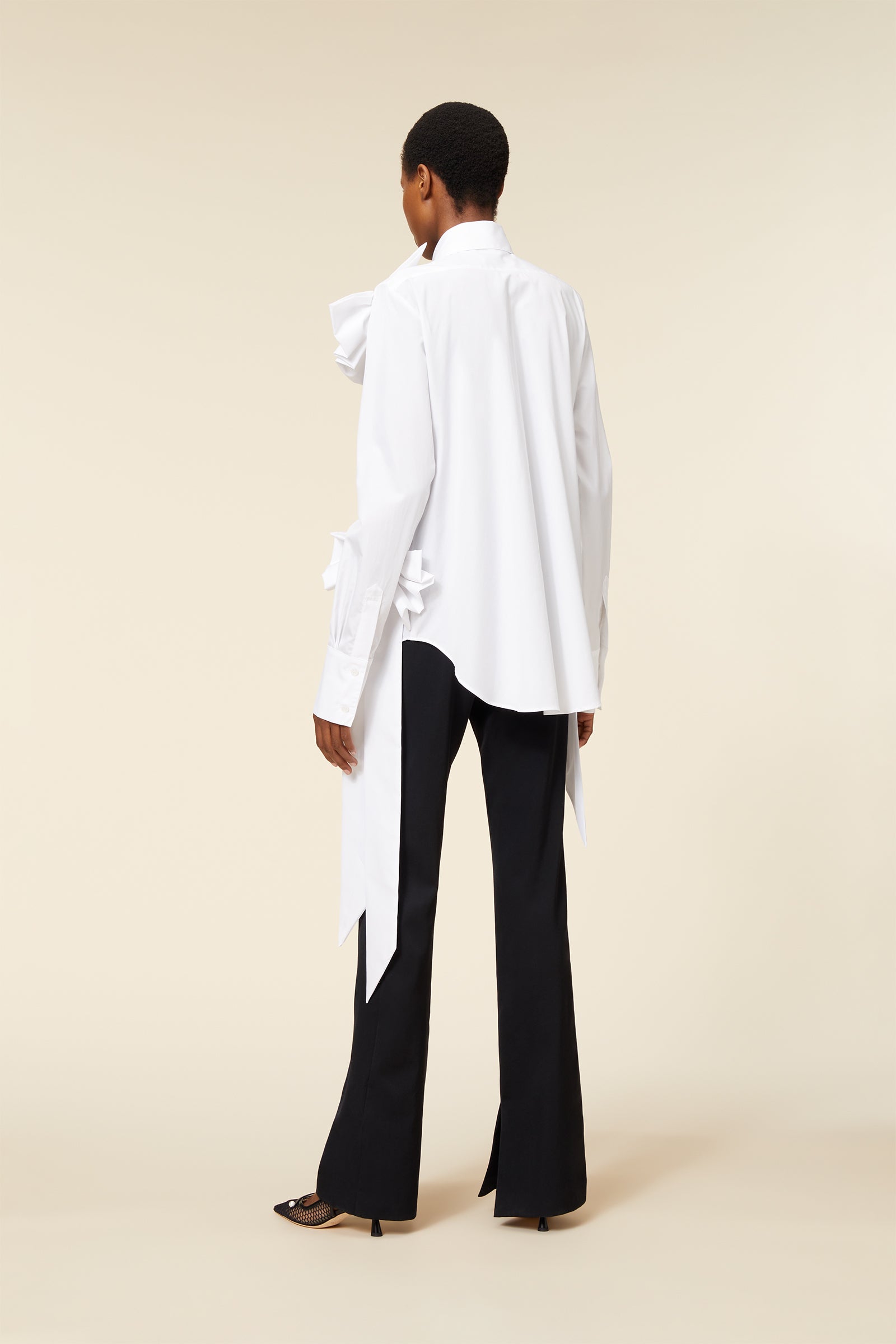 Fashion model in a stylish outfit featuring a unique white asymmetrical blouse and elegant black trousers.