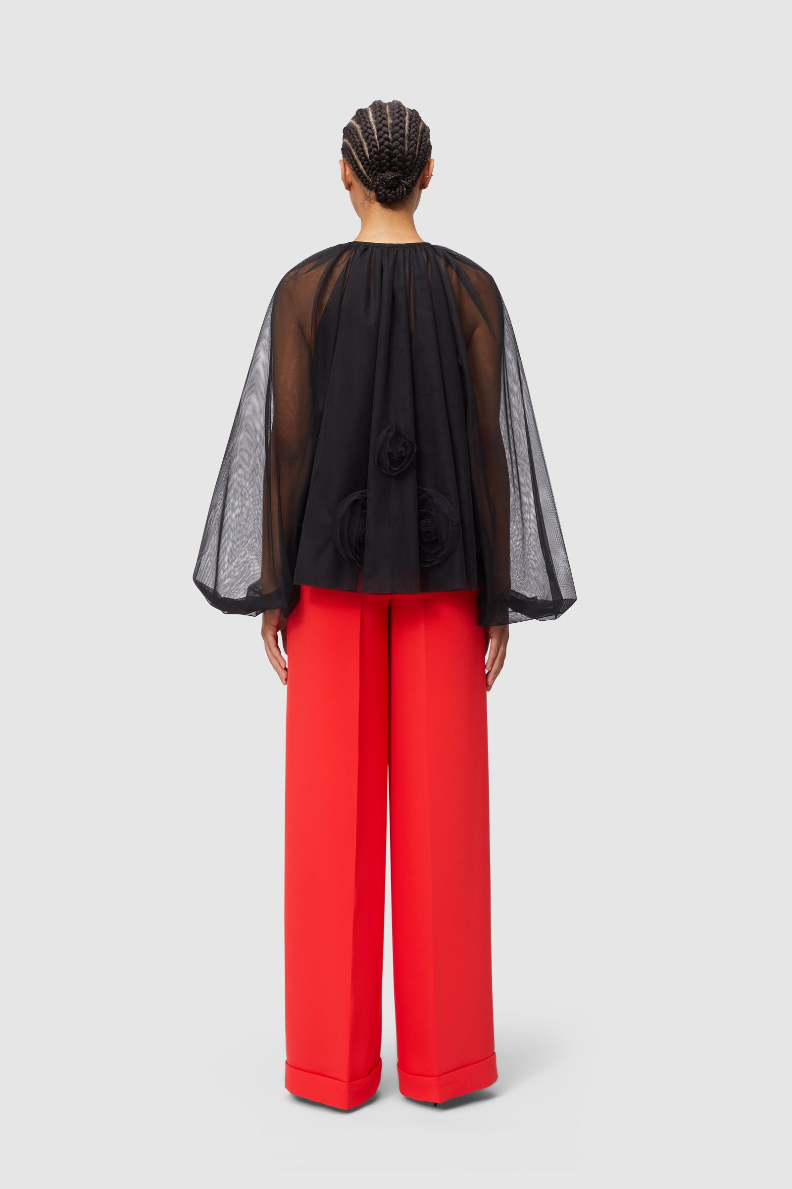 Sheer black blouse with textured floral details paired with vibrant red wide-leg trousers in a chic and modern ensemble.