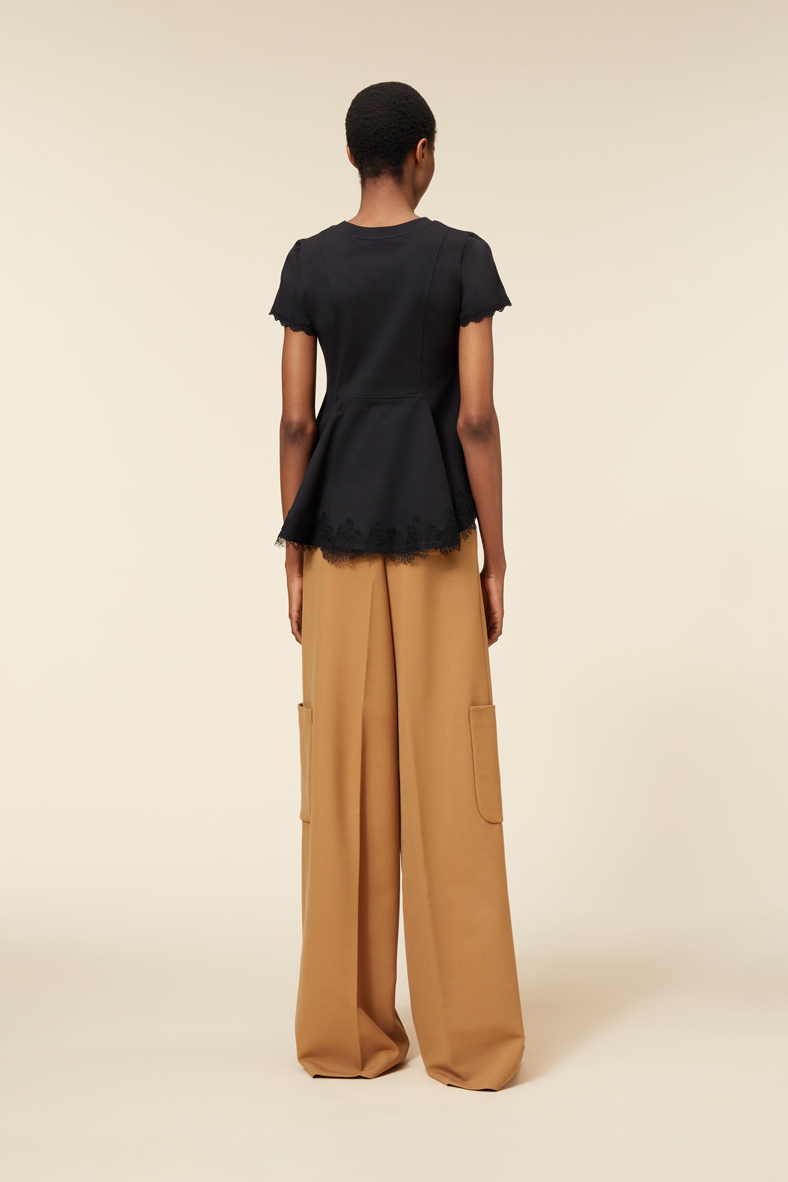 Black peplum top with lace trim paired with wide-legged, camel-colored trousers featuring large side pockets.