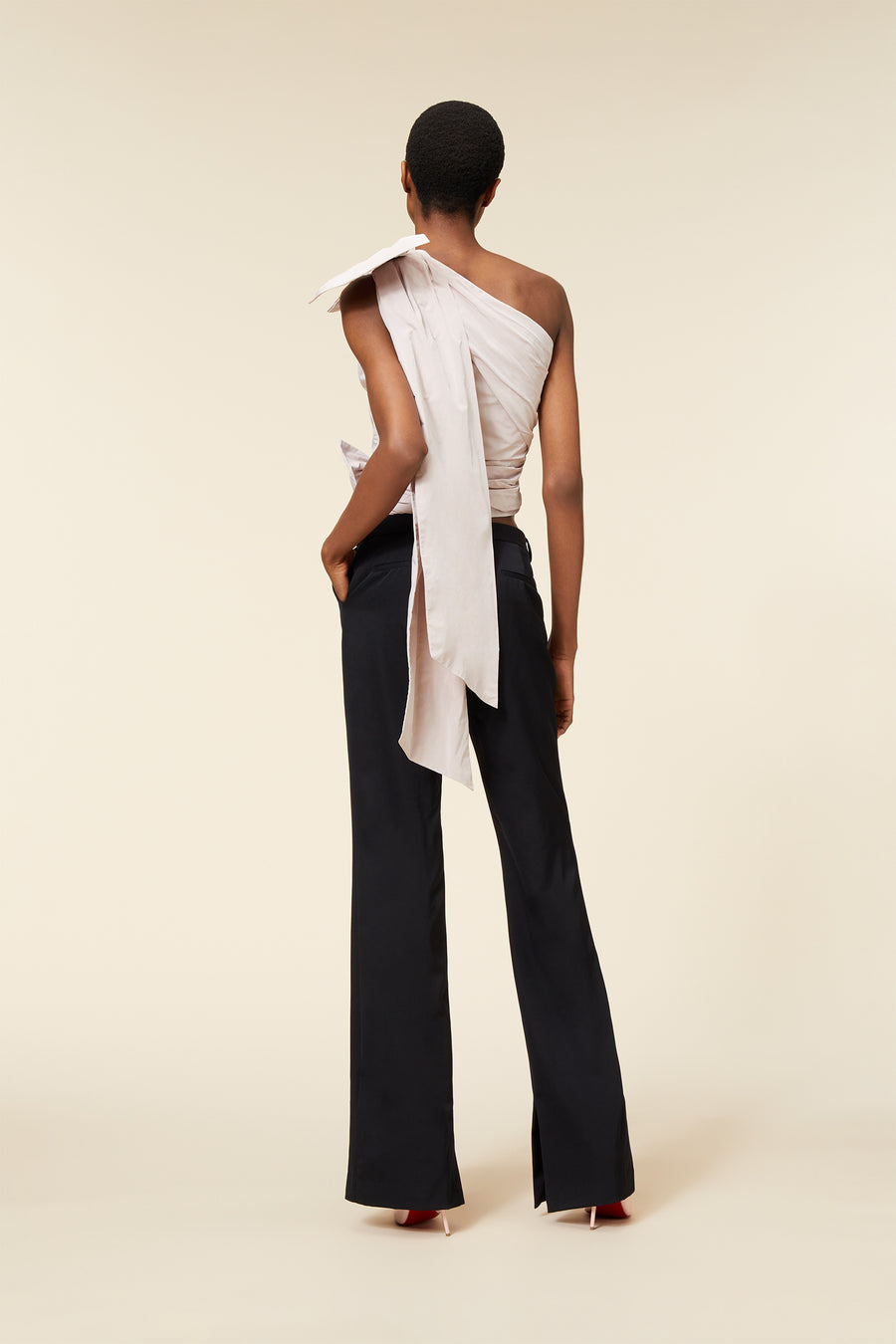 Elegant woman wearing a sophisticated, asymmetrical white top with bow detail paired with classic black trousers.