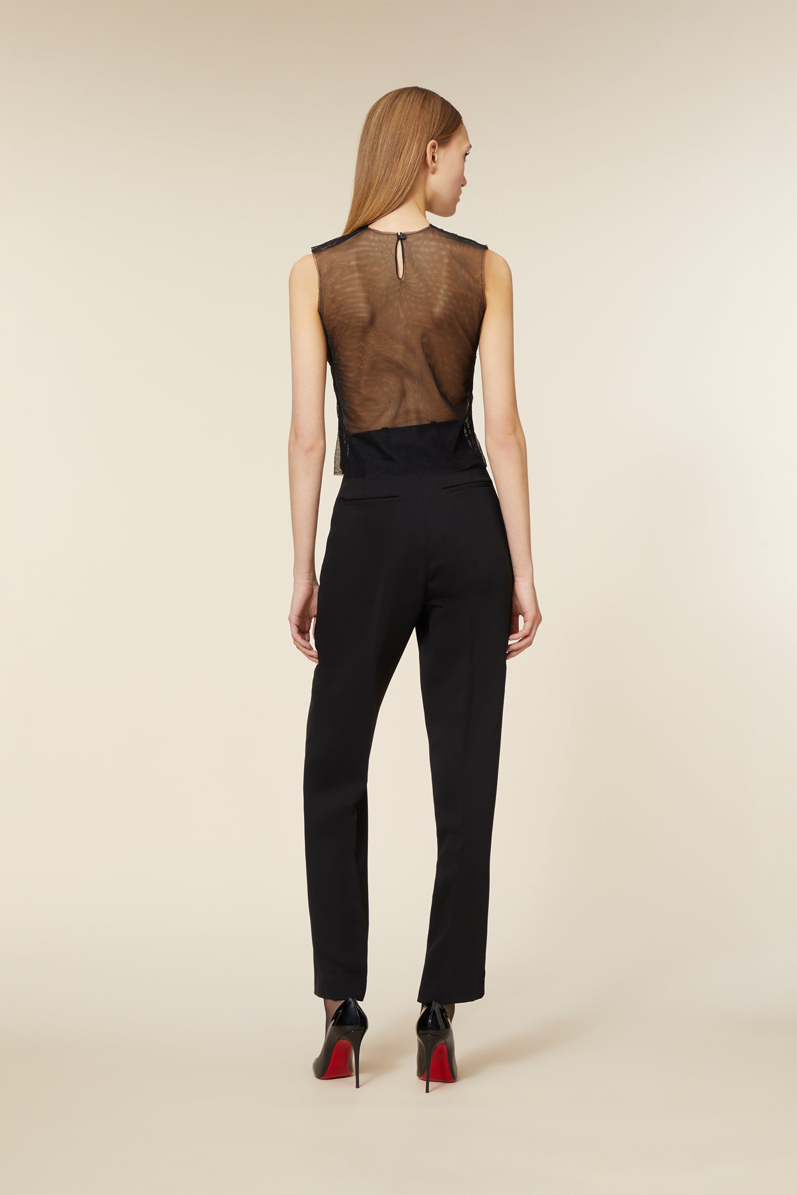 Woman wearing a stylish black see-through top with black dress pants and red-soled stiletto heels, posing elegantly.