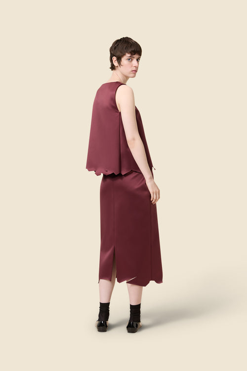 Elegant burgundy ensemble with asymmetrical top and midi skirt featuring subtle slit details against a minimalist backdrop.