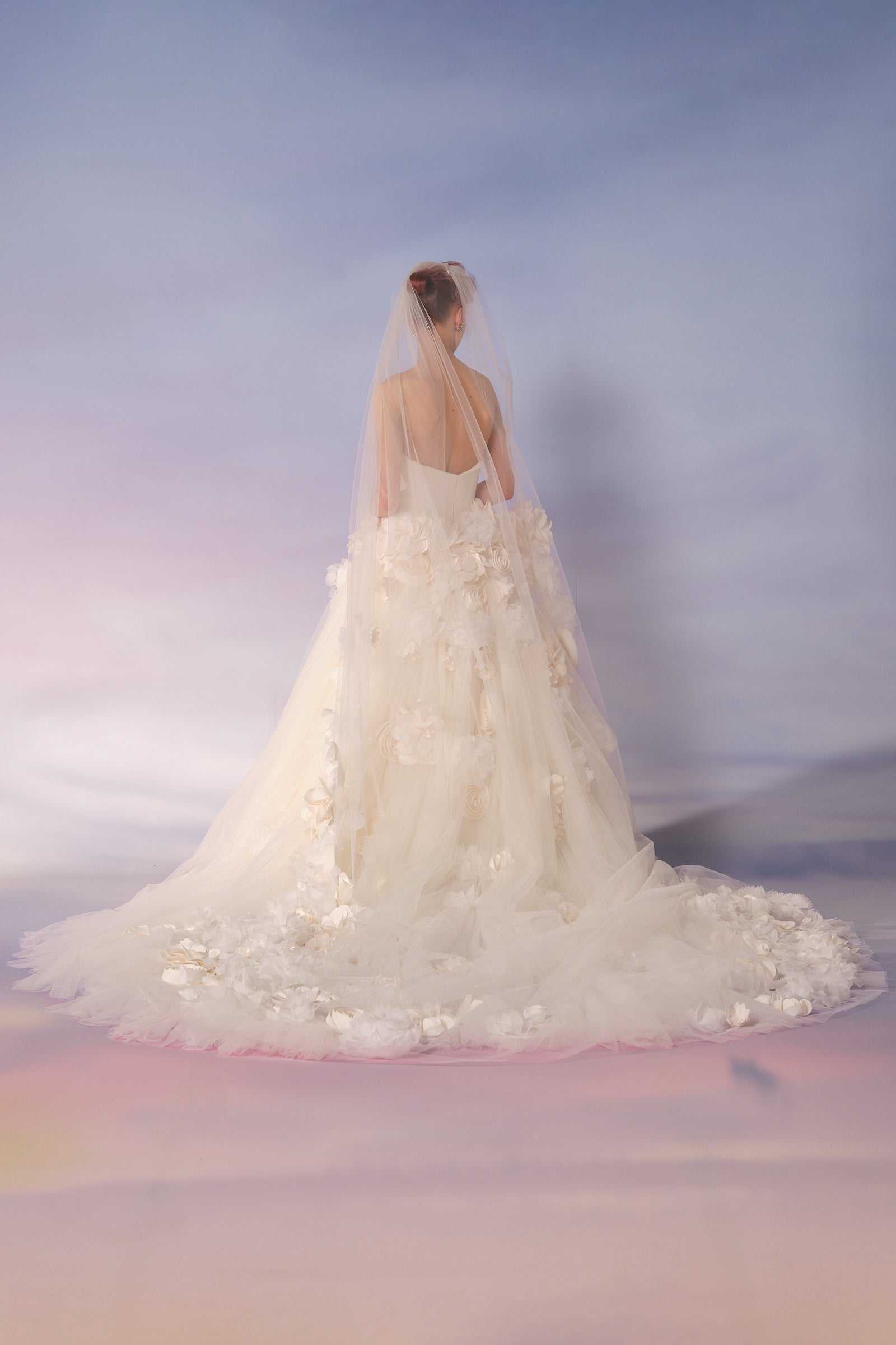 This tulle veil is adorned with meticulously handcrafted flower bouquets cascading gracefully down its length, for an ethereal and dramatic look, from the Viktor&Rolf Mariage collection.