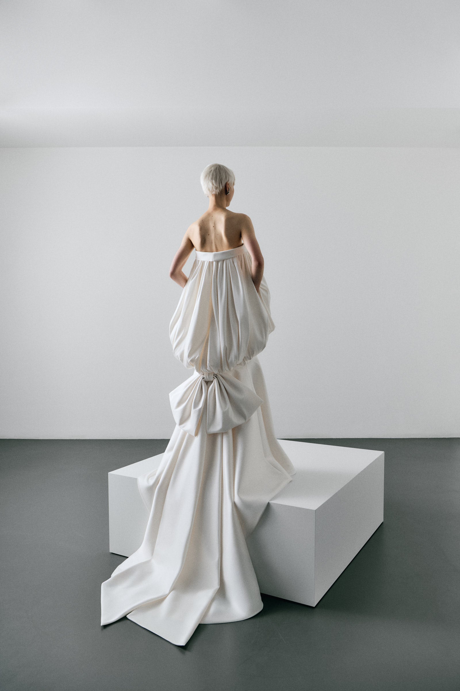 White sculpture of a draped garment on a pedestal in a minimalistic setting
