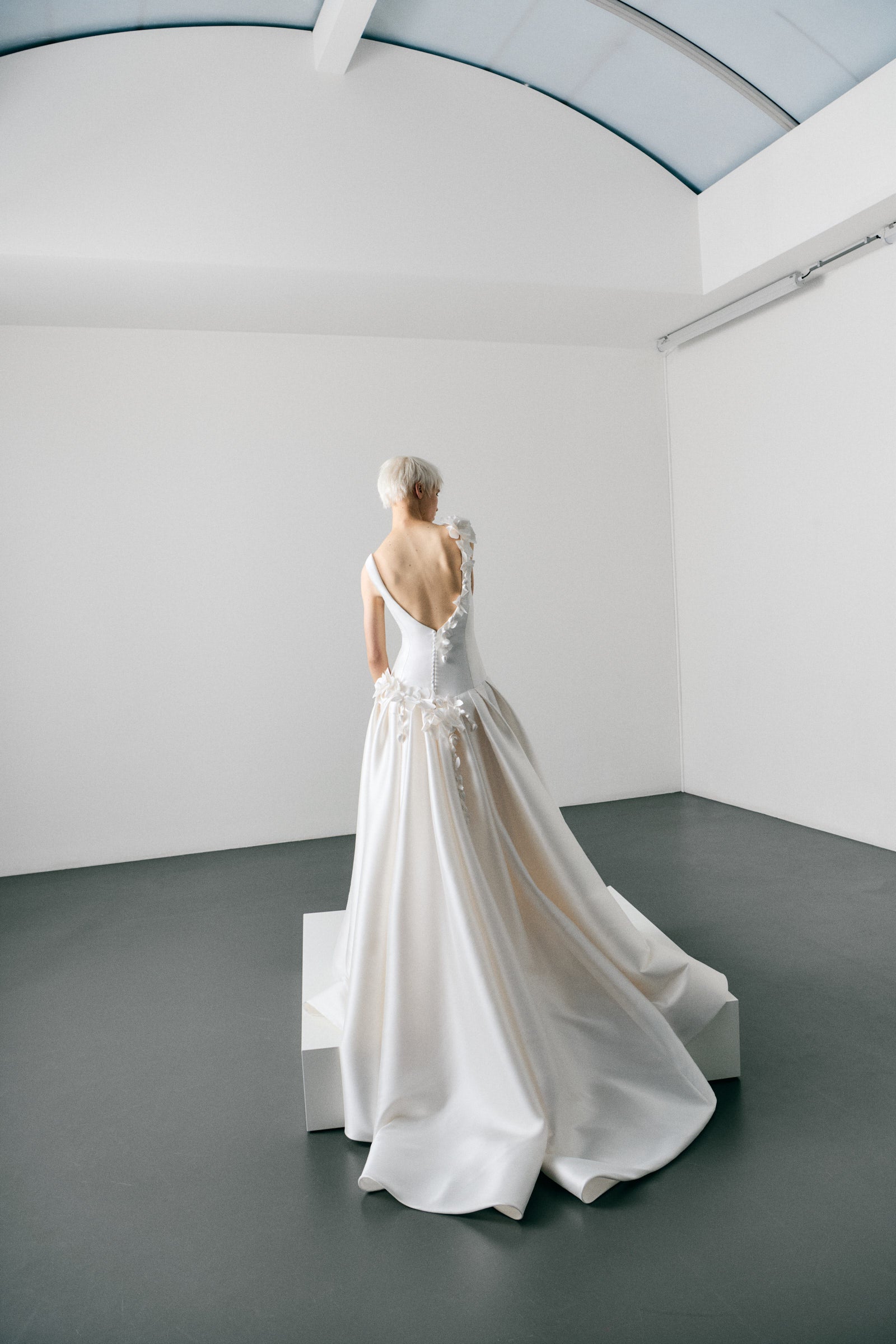 White wedding dress on a model in a minimalistic room with white walls and grey floor.
