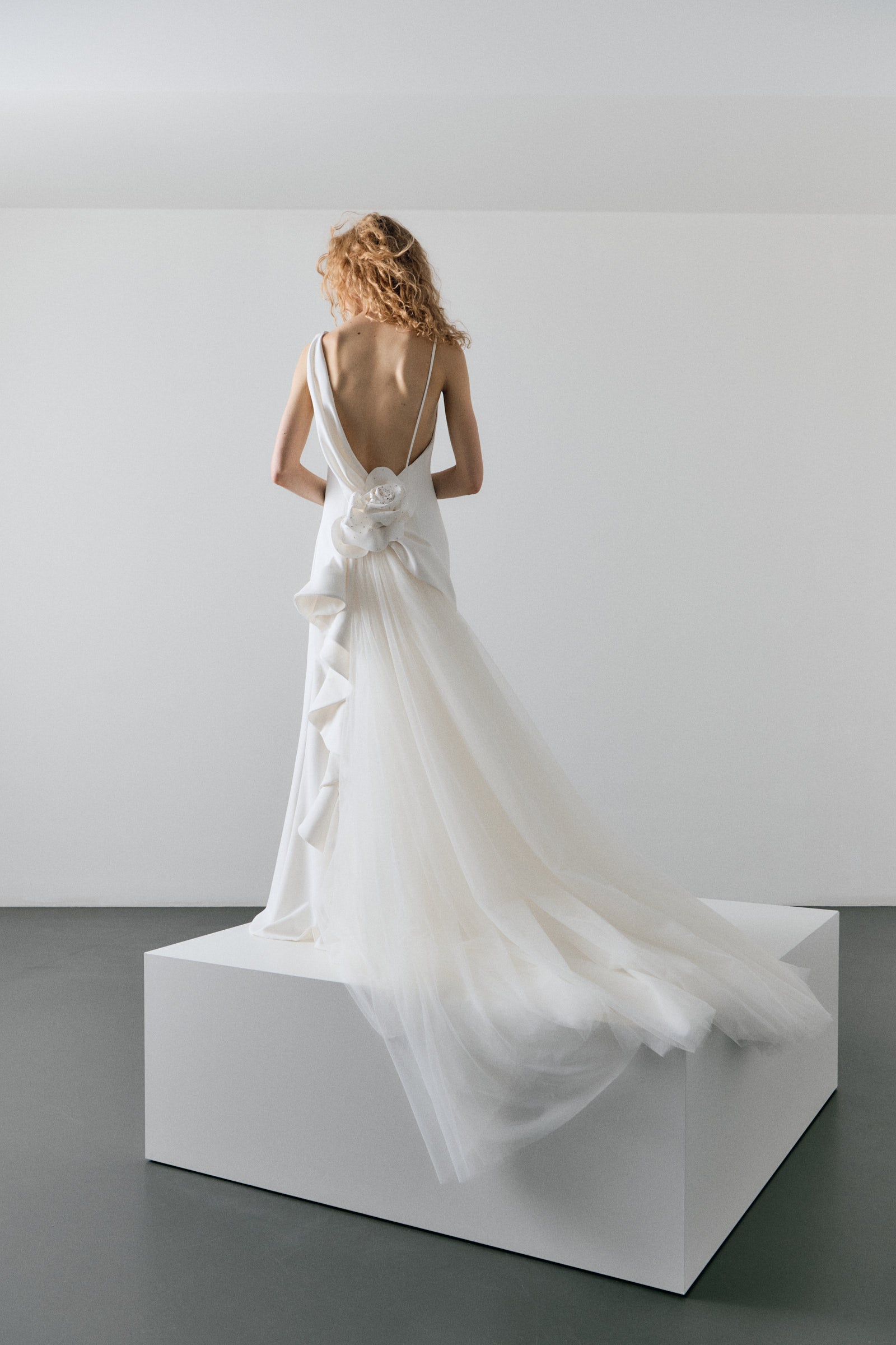 Woman in a white wedding dress standing on a white platform against a plain background