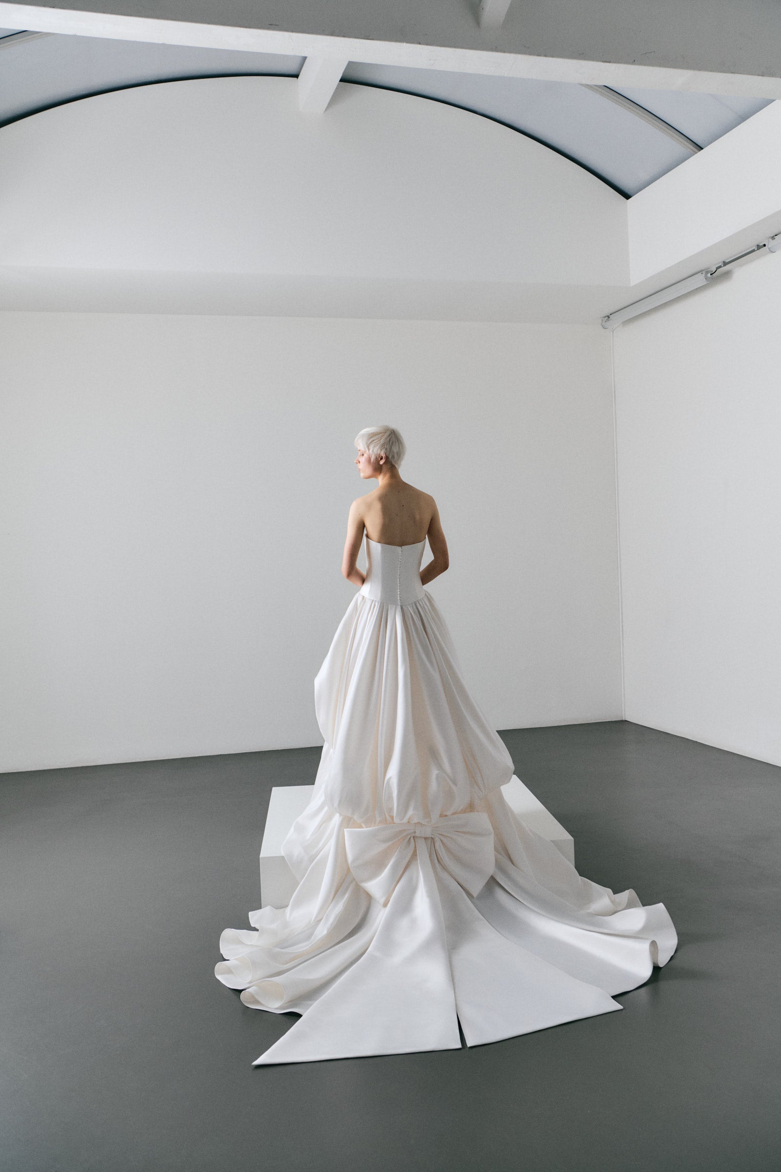 Model wearing a white strapless wedding gown with ruffled bottom on a white background.
