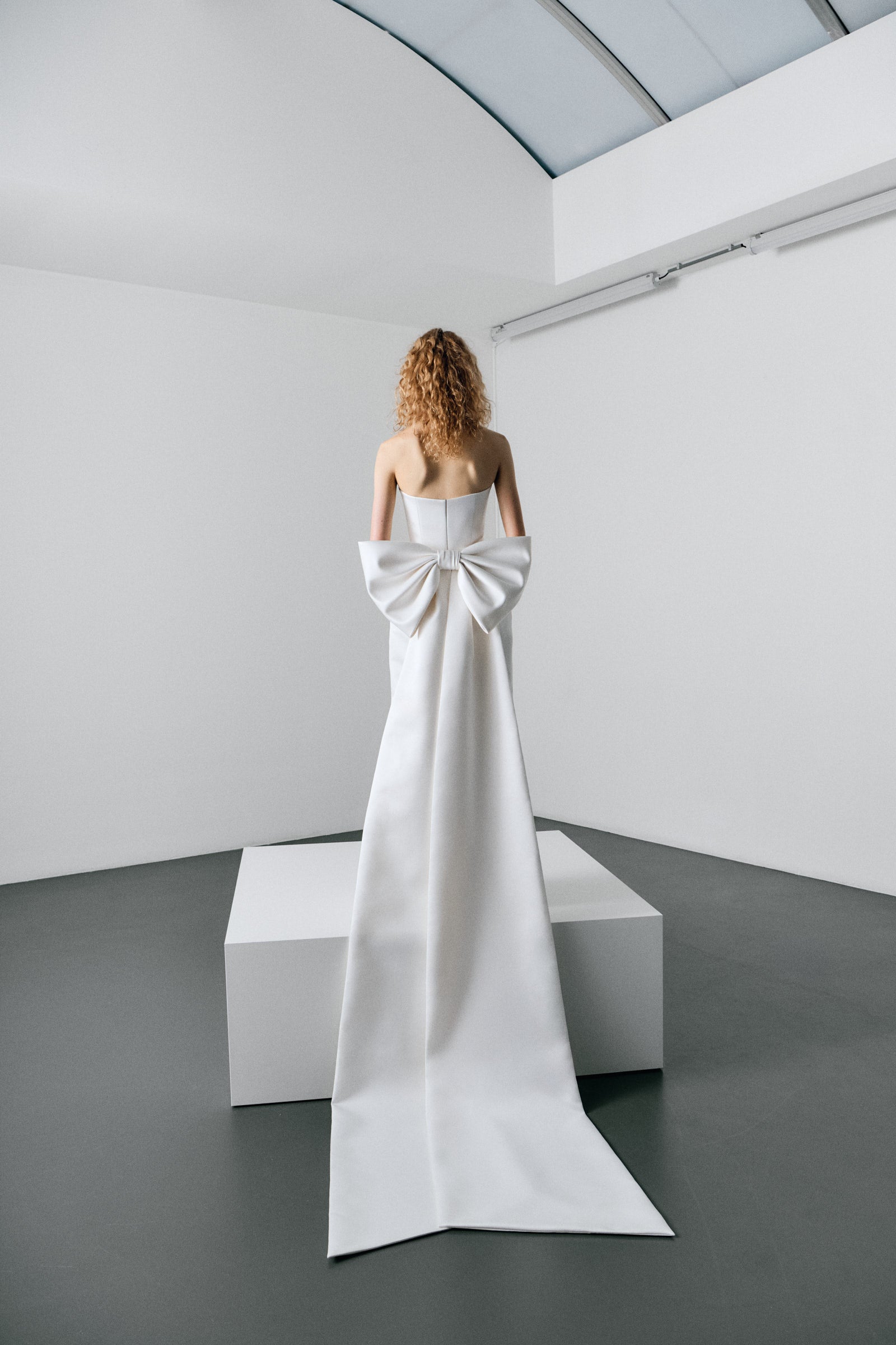 Woman wearing a white strapless gown with ruffled layers on a white platform.