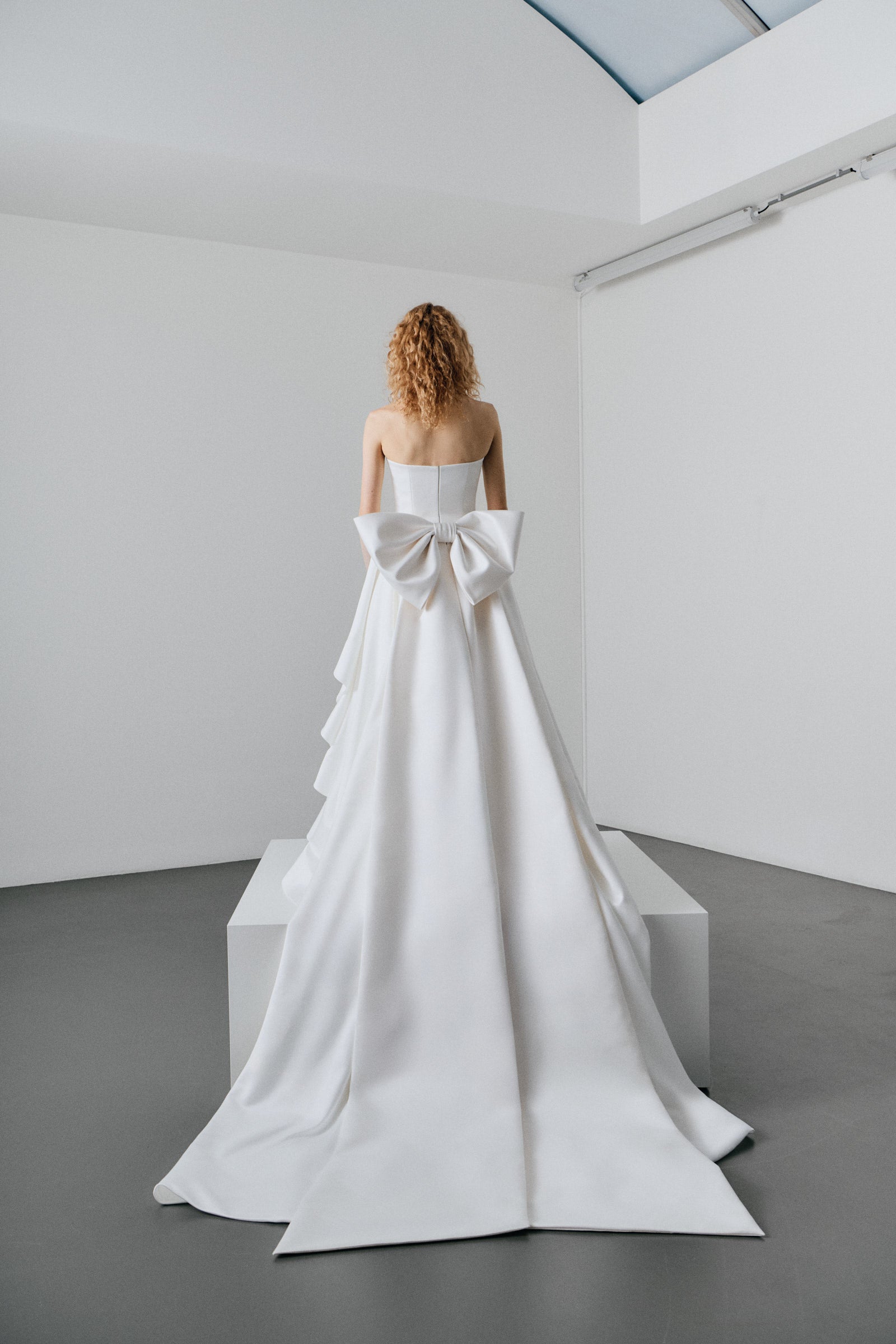 Woman wearing a white strapless gown with ruffled layers on a white platform.