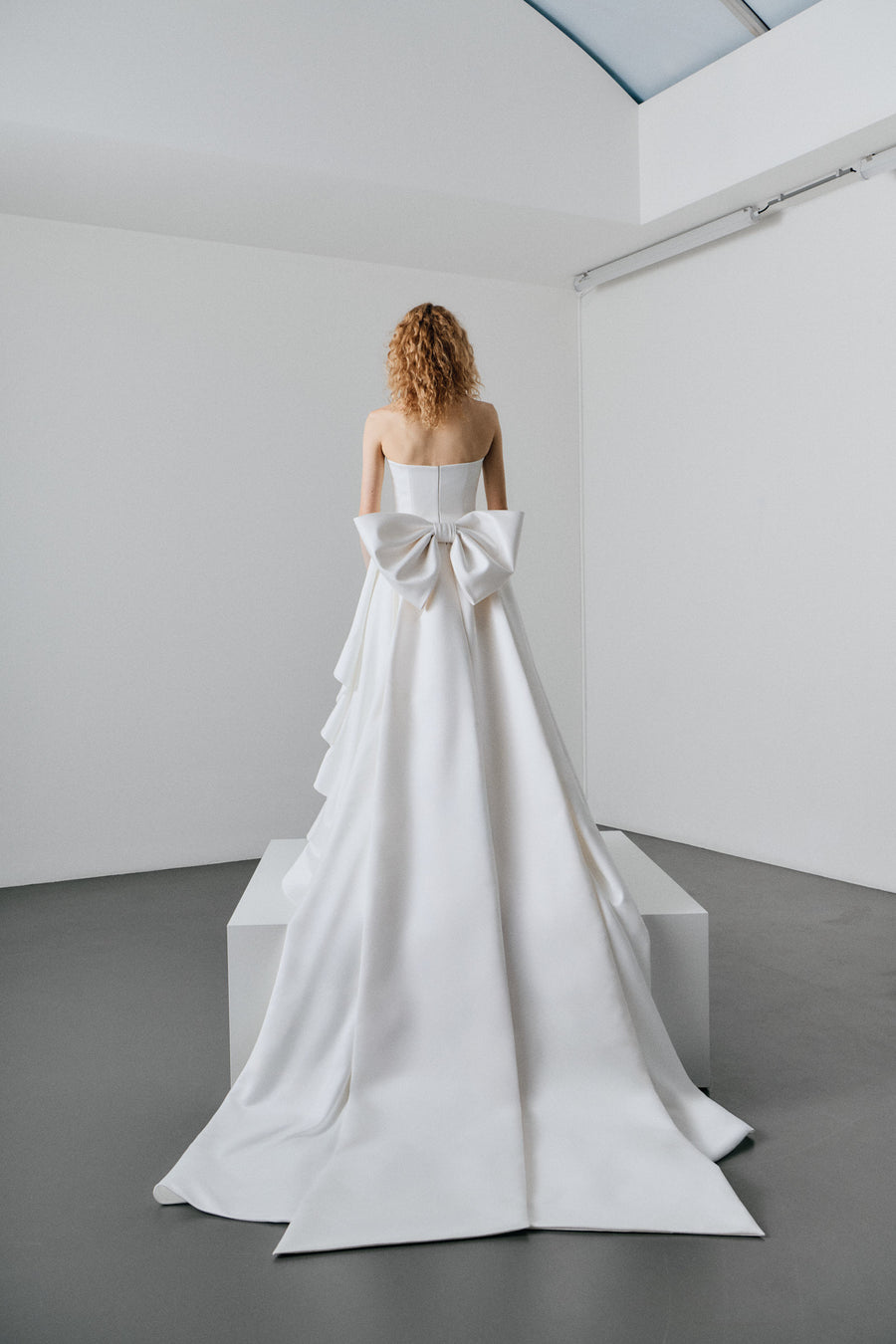 Woman wearing a white strapless gown with ruffled layers on a white platform.