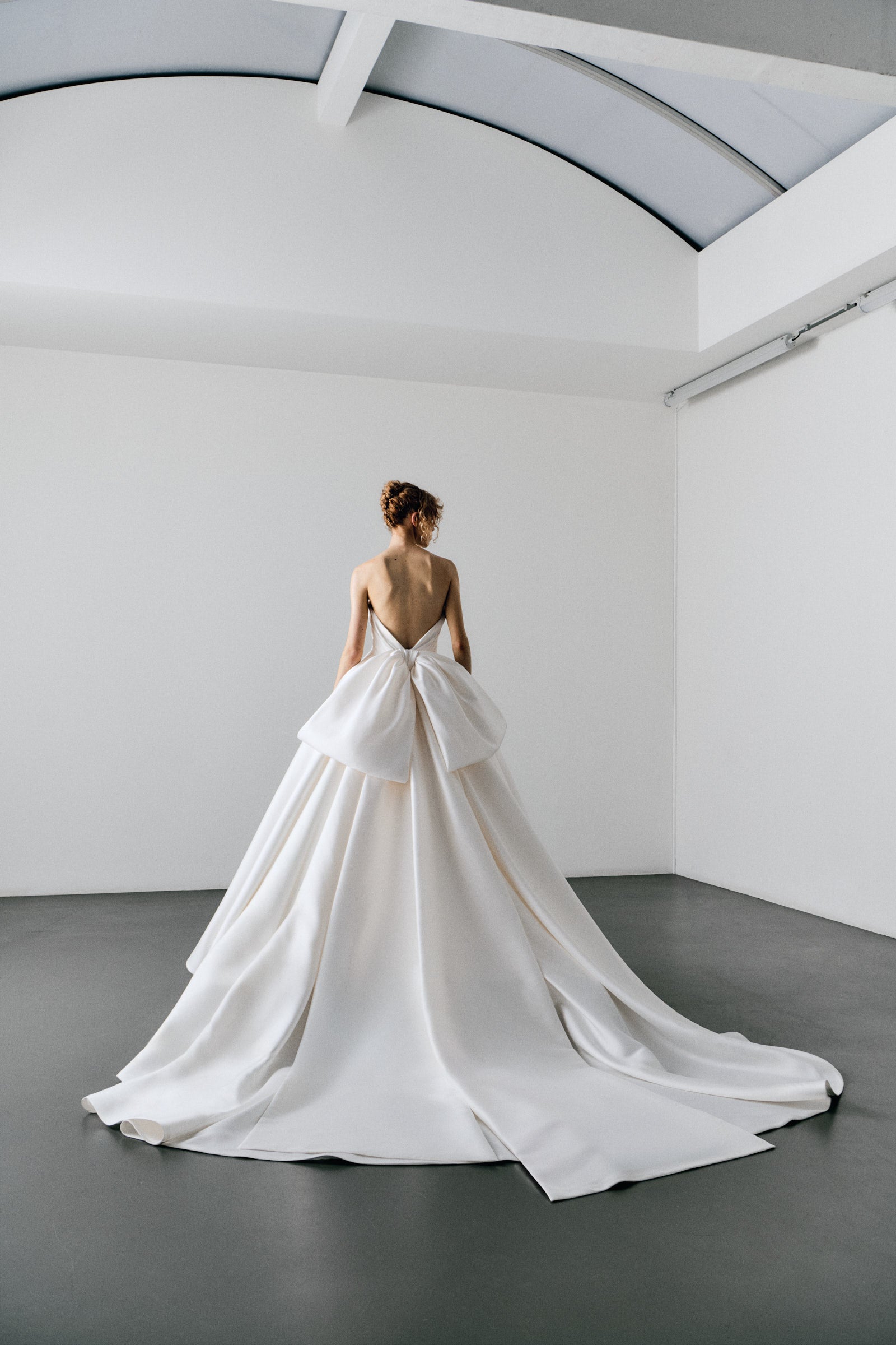 Woman in a white wedding dress standing on a platform in a minimalistic room.