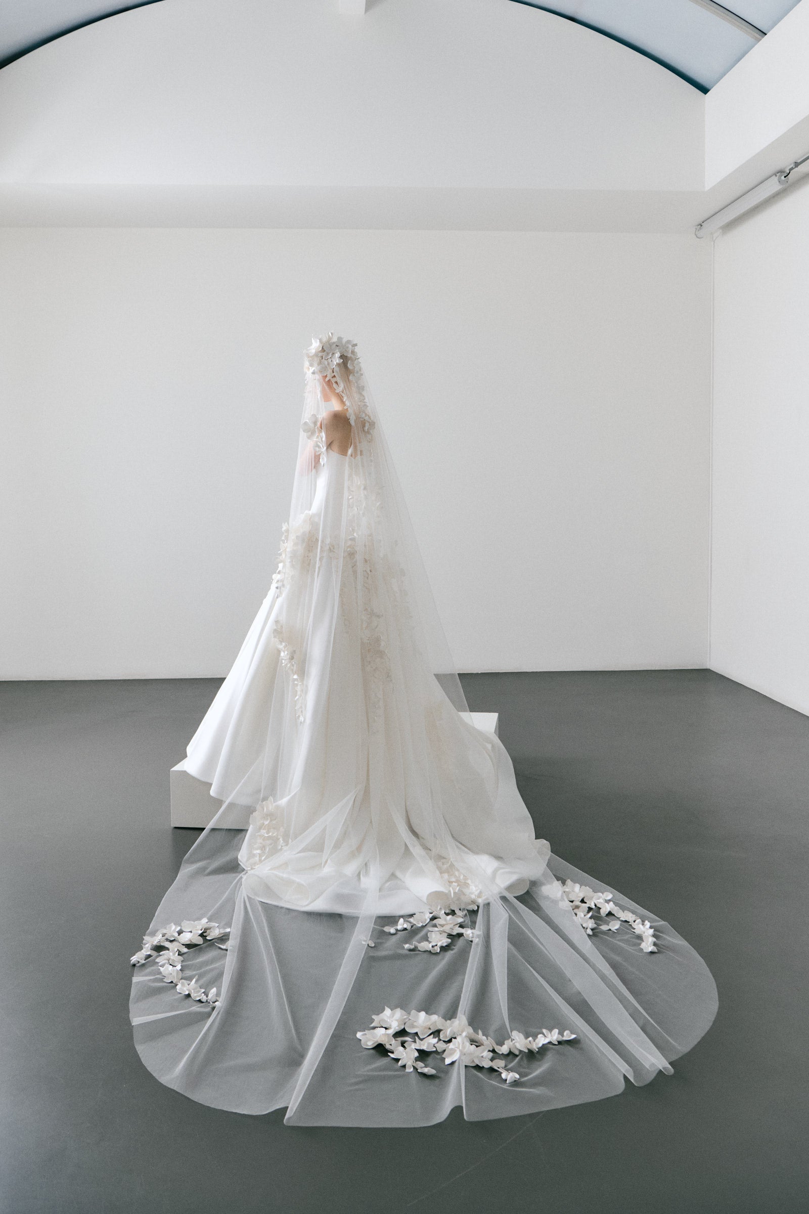 White wedding dress with floral details and a long veil on a plain background