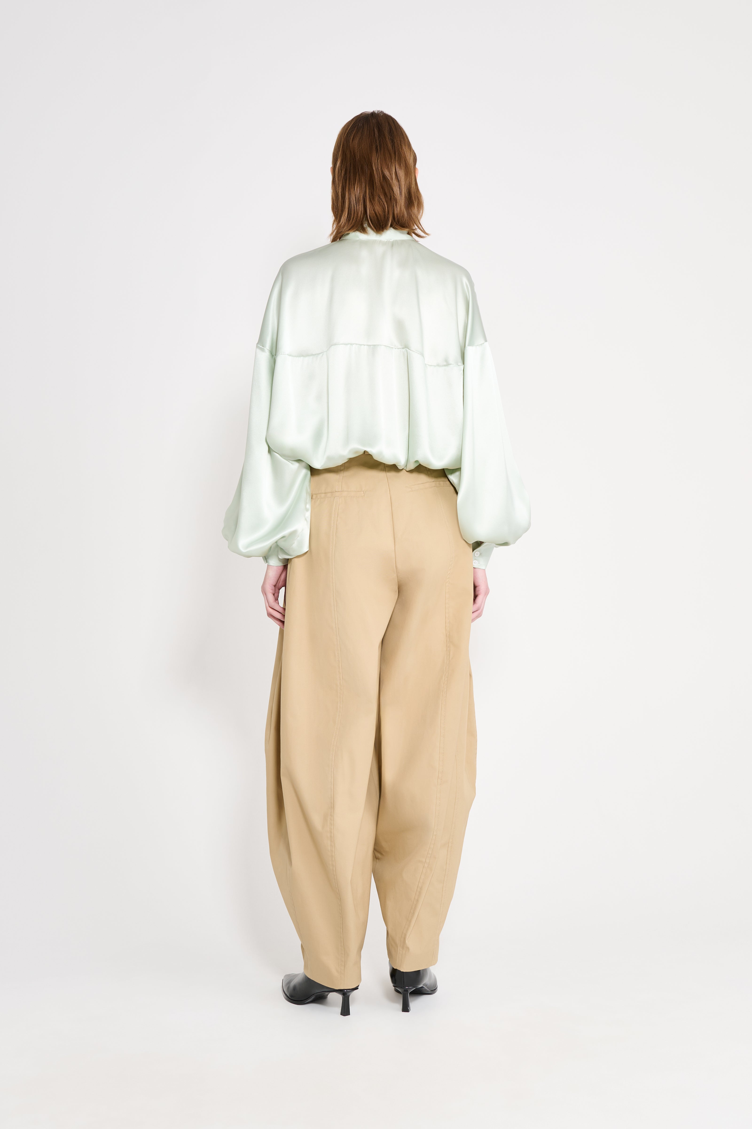 Person wearing a light green blouse and beige pants on a white background