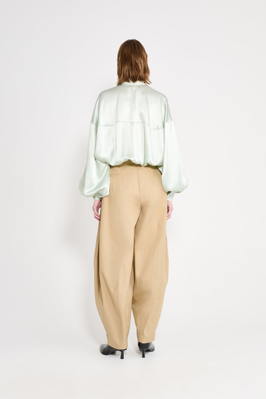 Person wearing a light green blouse and beige pants on a white background