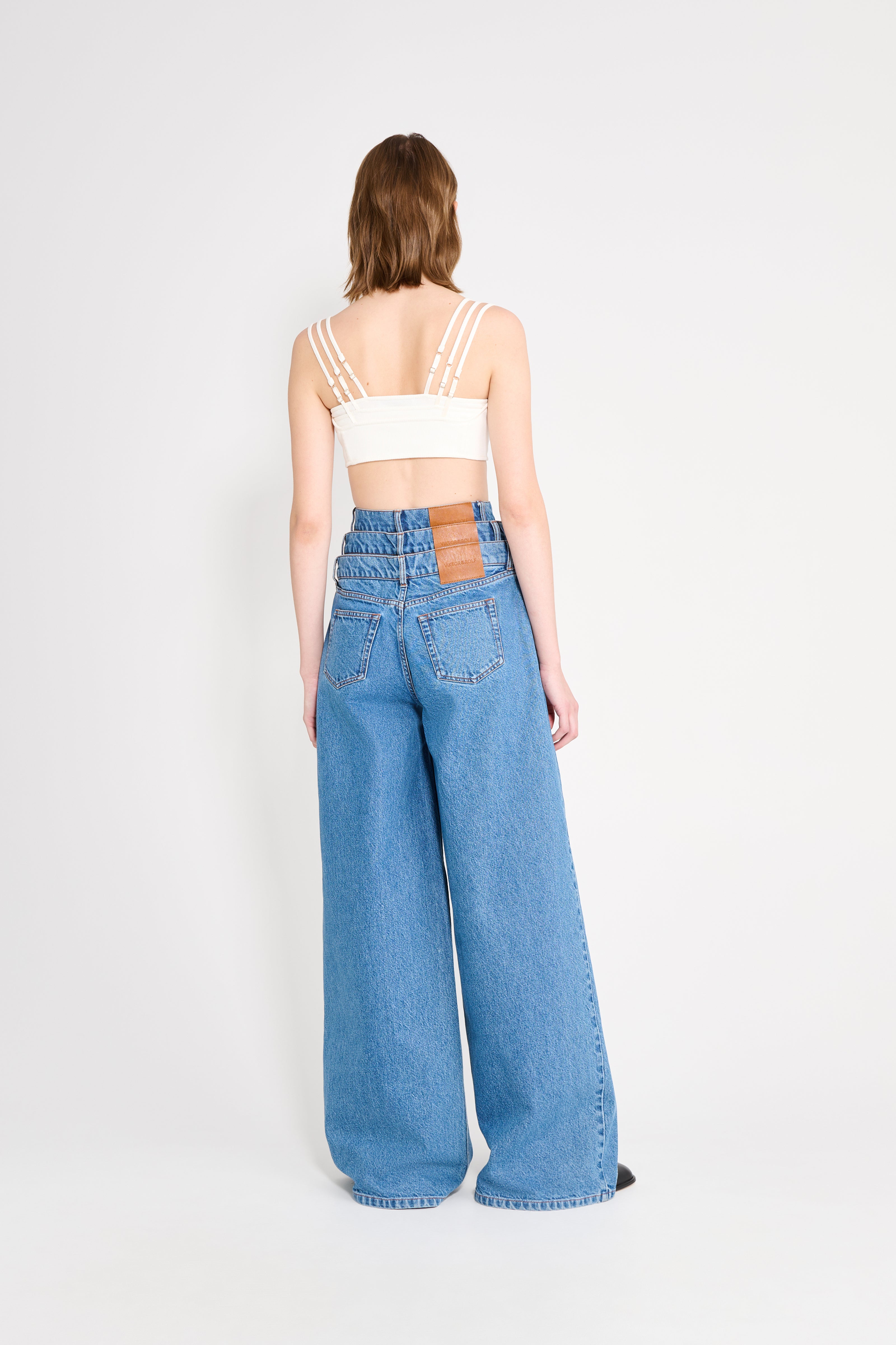 Person wearing a white crop top and blue high-waisted jeans on a white background
