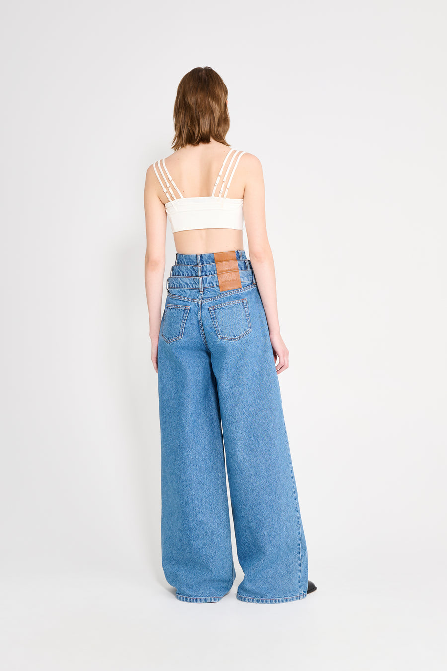 Person wearing a white crop top and blue high-waisted jeans on a white background