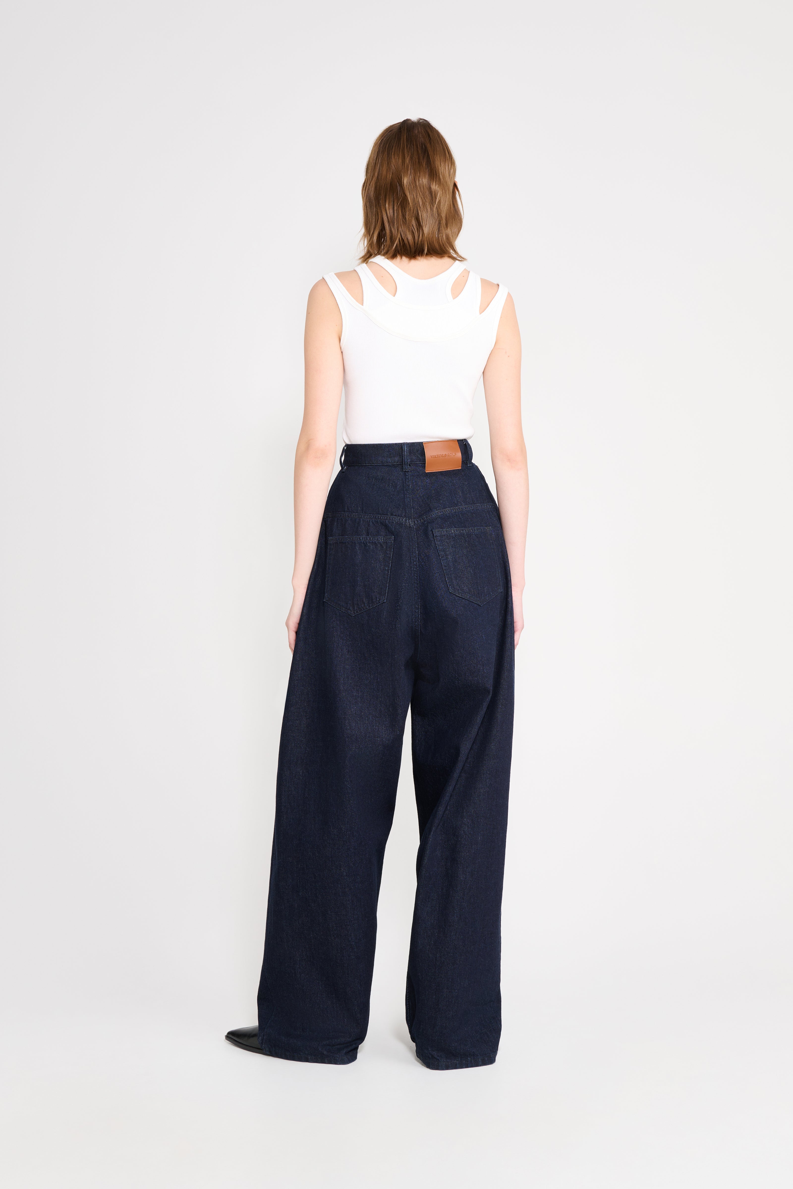 Person wearing navy wide-leg pants and a white sleeveless top on a light gray background