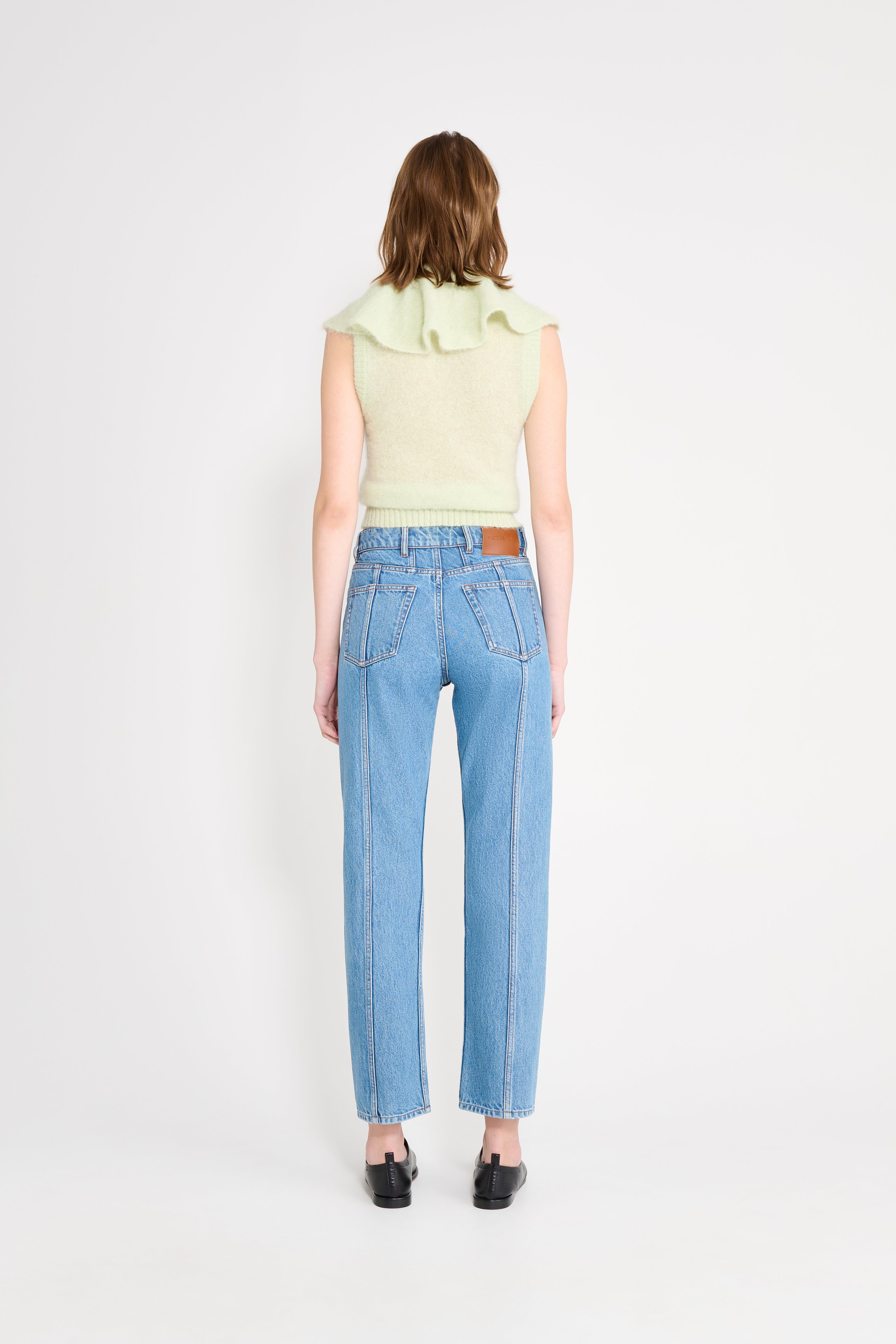 Woman wearing light blue jeans and a light green sleeveless top on a white background