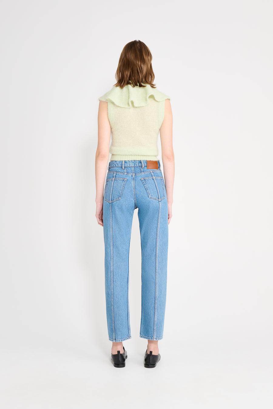 Woman wearing light blue jeans and a light green sleeveless top on a white background