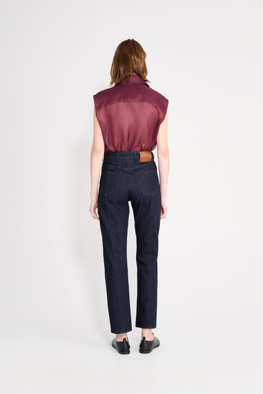 Person wearing a burgundy sleeveless top and dark jeans on a white background