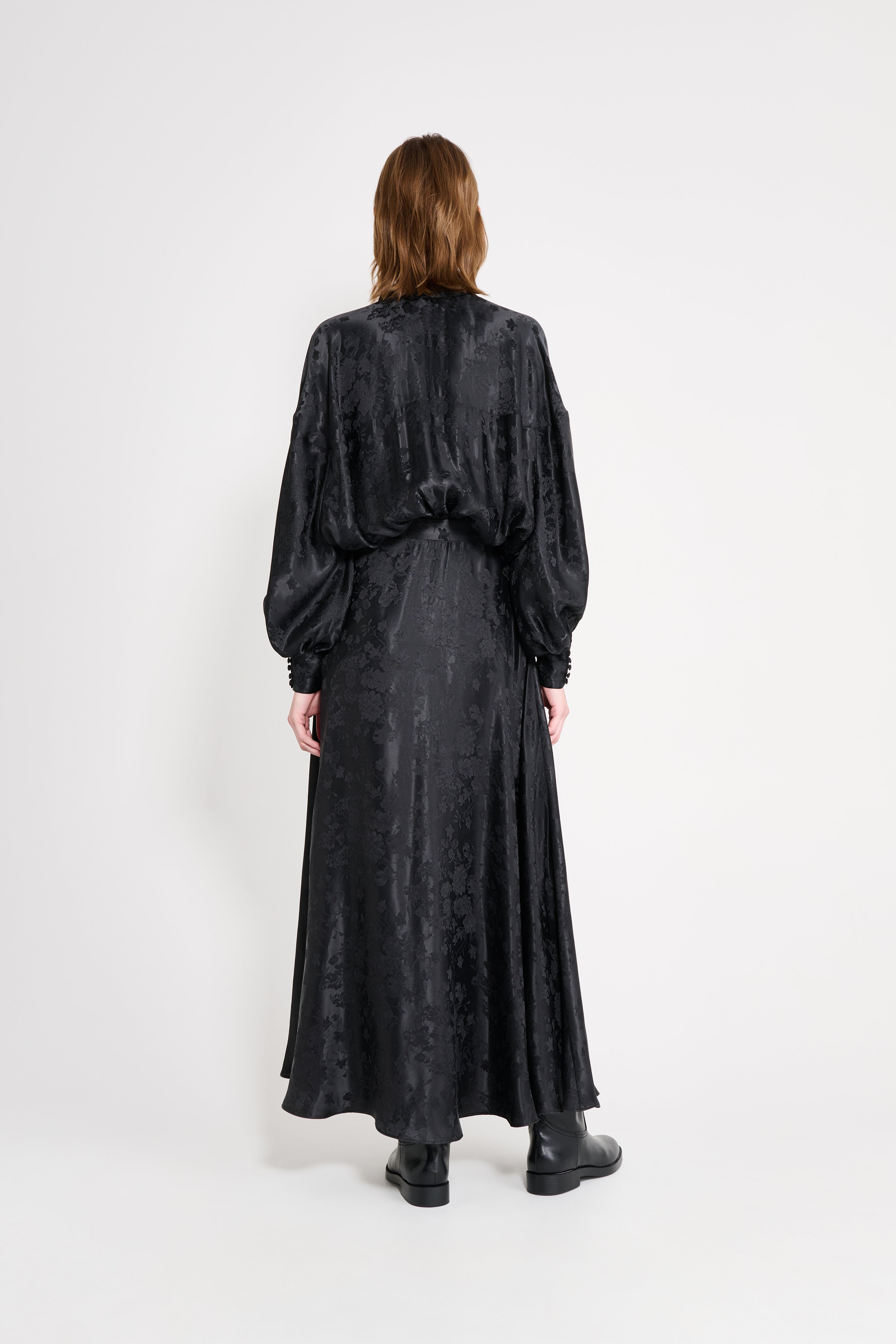 Person wearing a long black dress with a plain white background