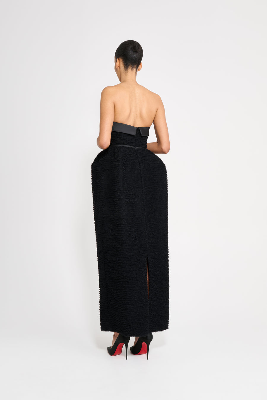 Woman wearing a black strapless gown with a slit on a white background