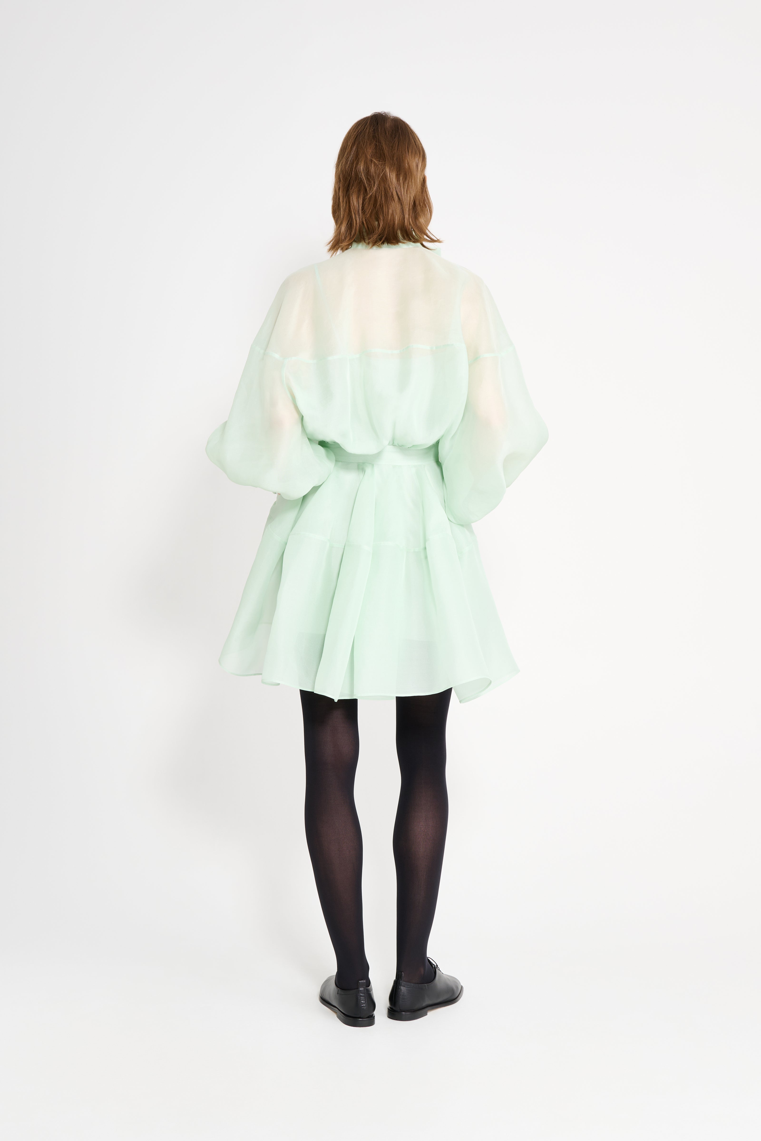 Person wearing a light green dress with a white background