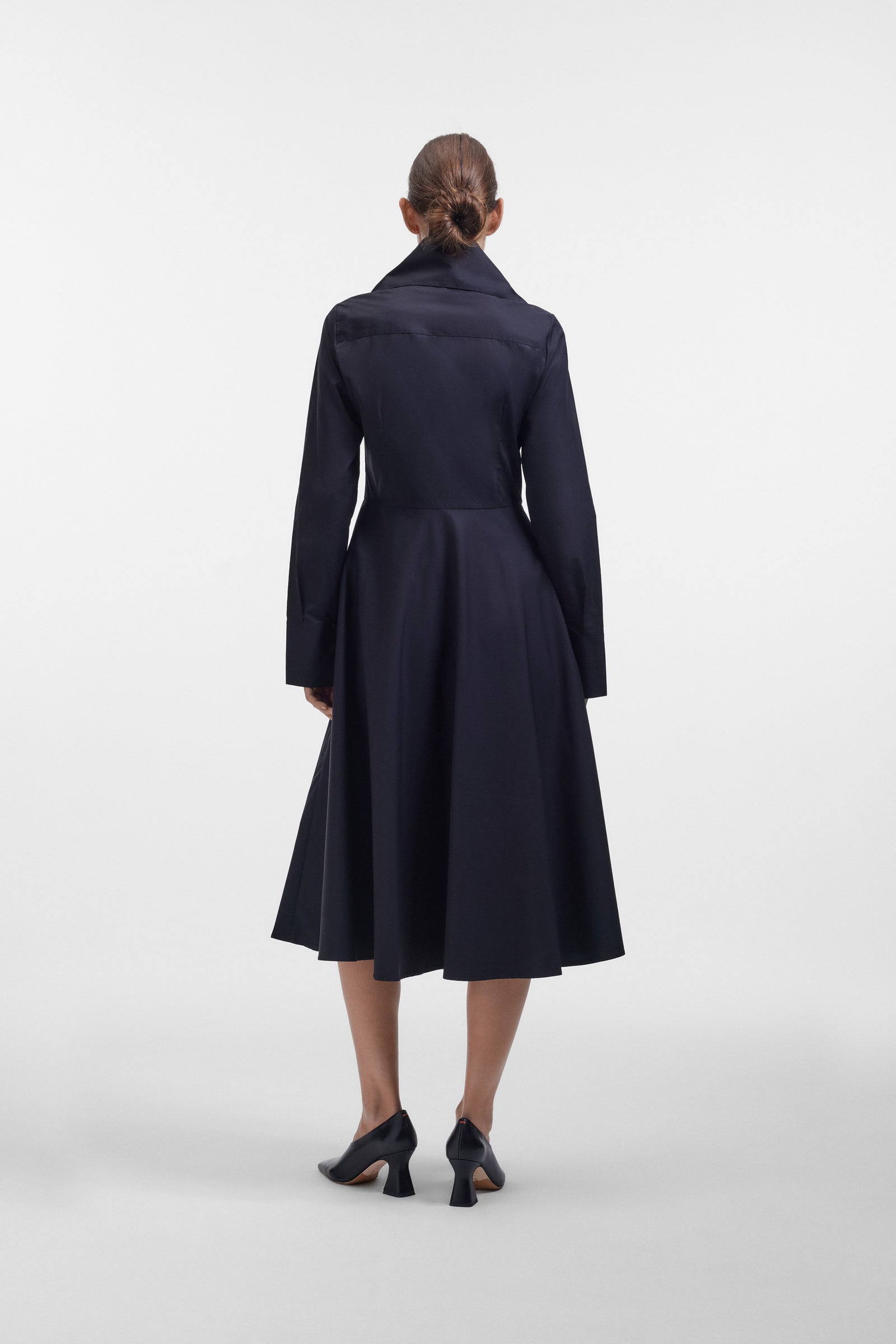 Model wearing a long black dress with a multi-layer collar and a bow detail on a white background.