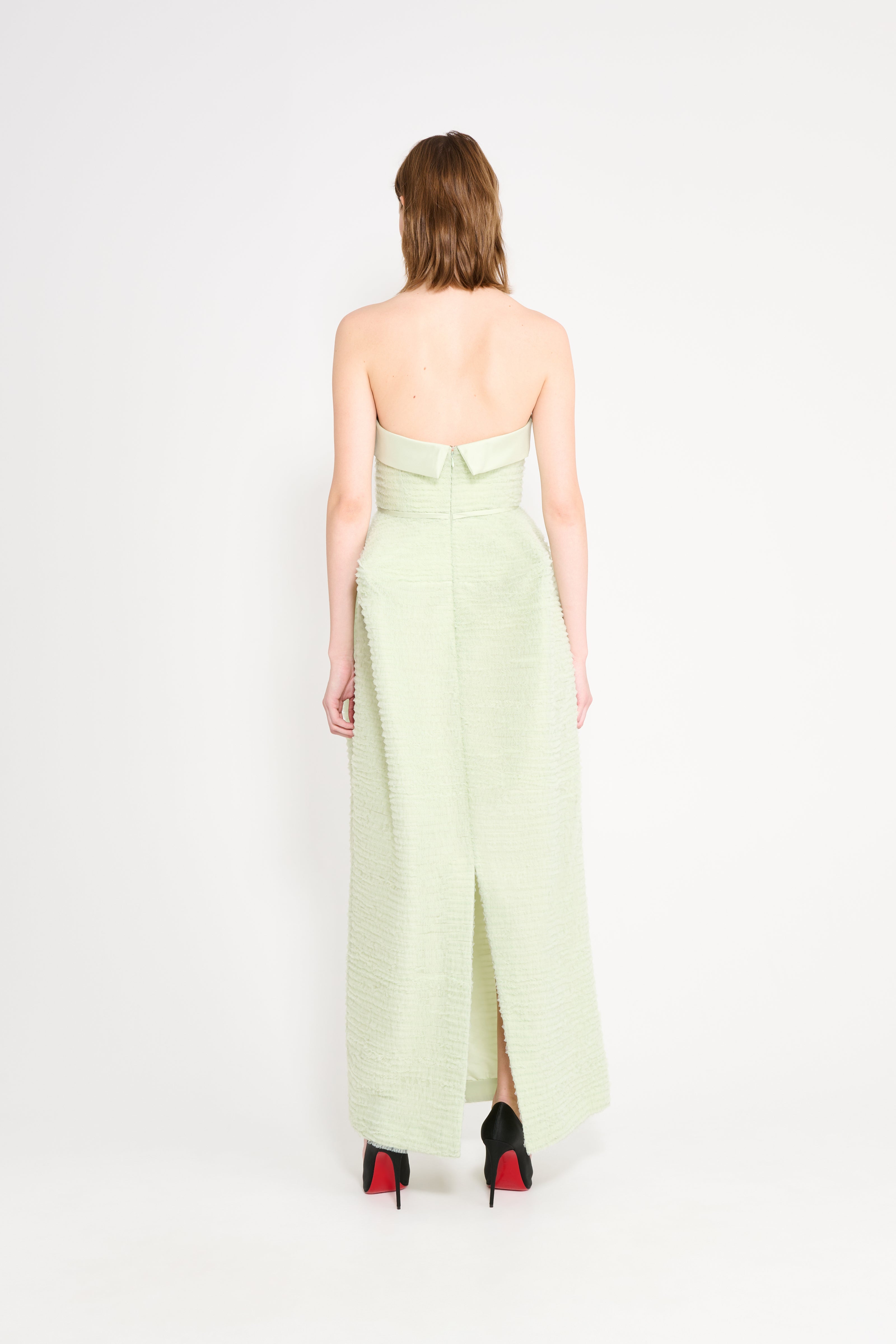 Woman wearing a light green strapless dress with a slit on a white background