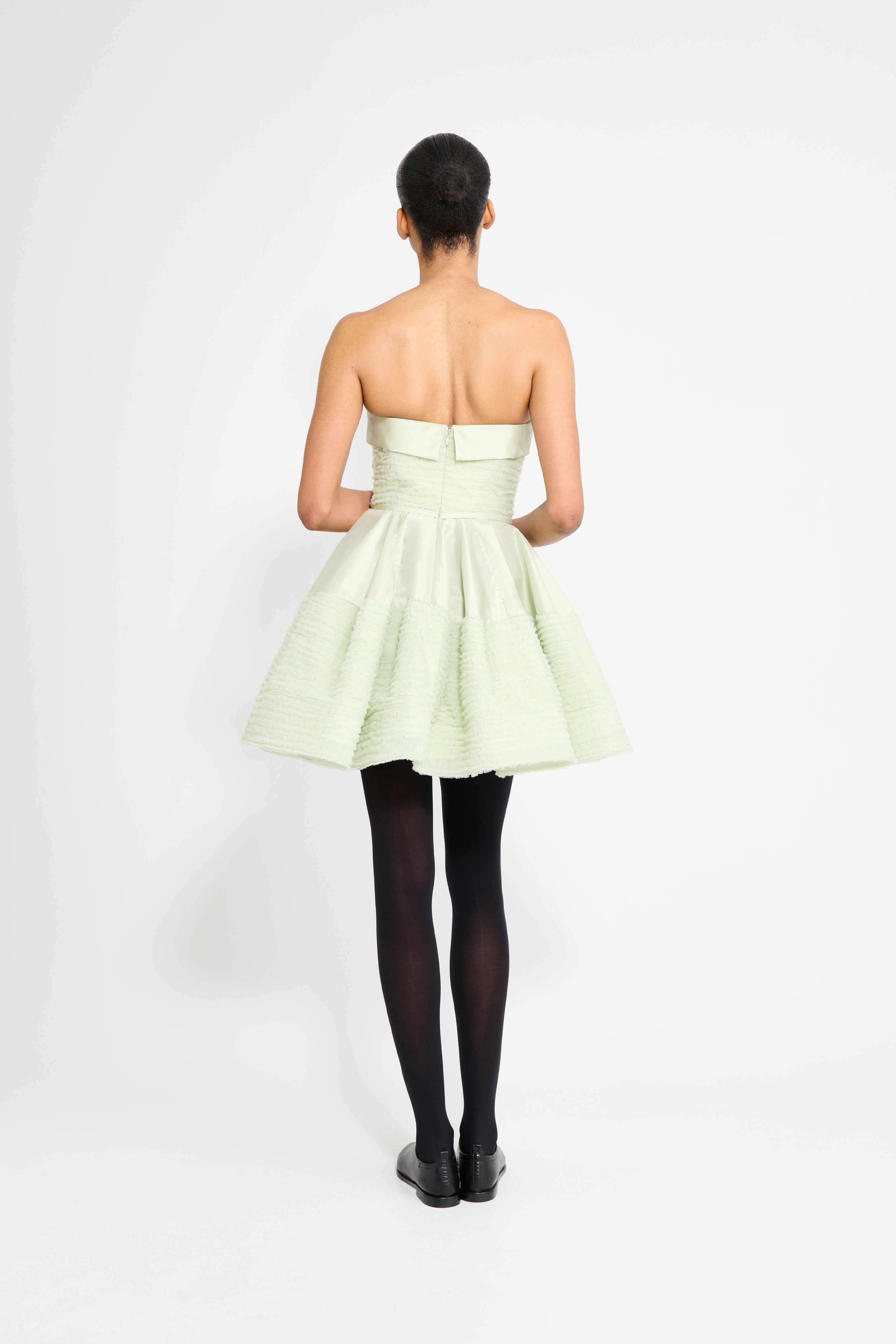 Woman wearing a light green strapless dress on a white background