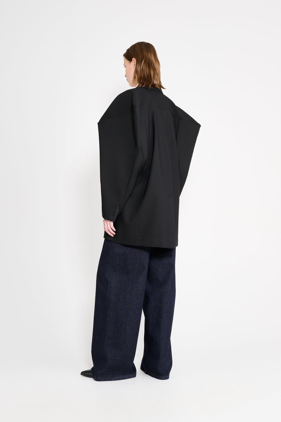 Model wearing a black square blazer shown from the back.