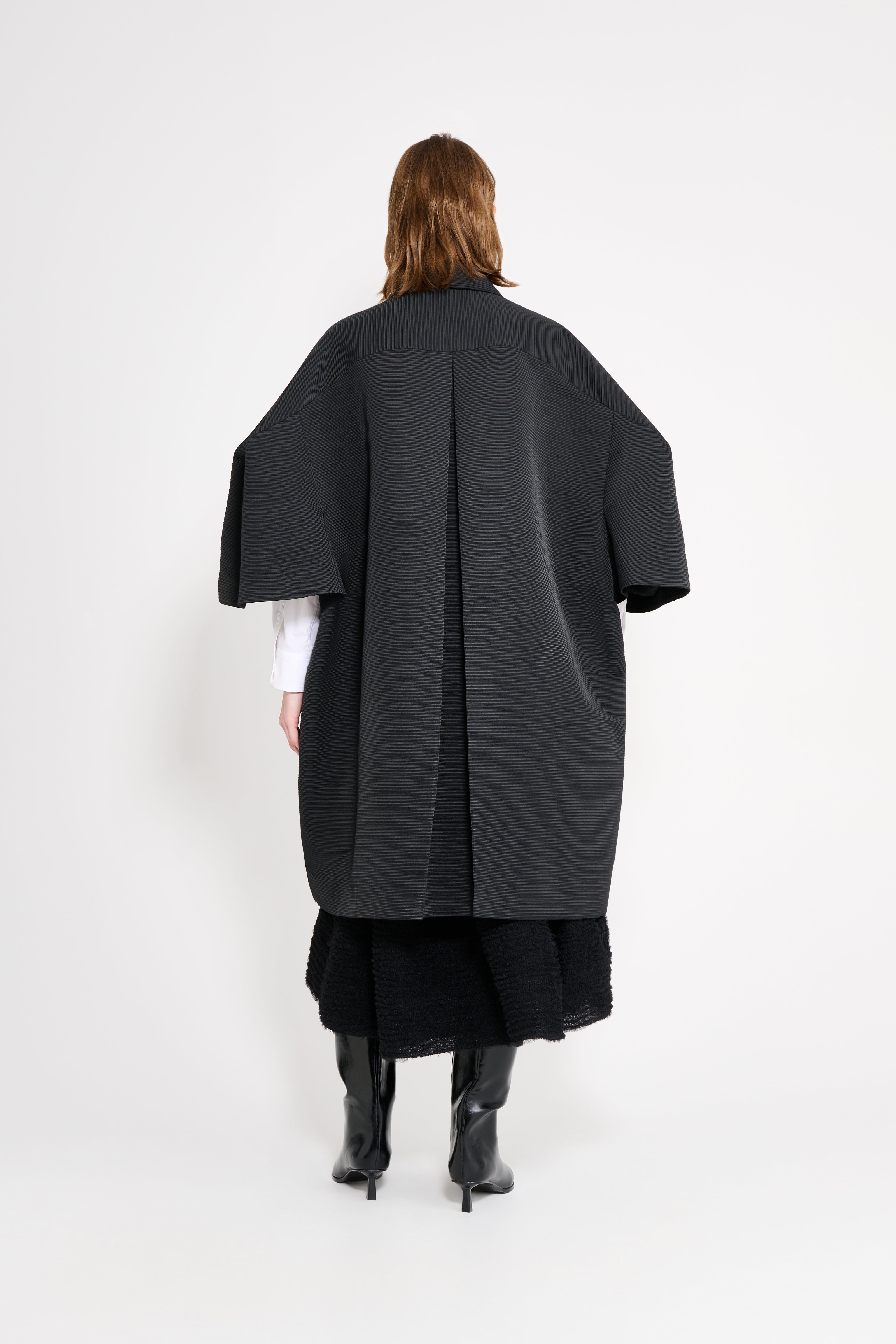 Person wearing a long black coat on a white background