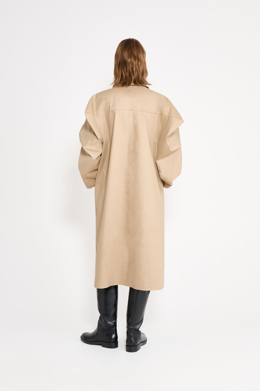 Person wearing a beige coat and black boots on a white background