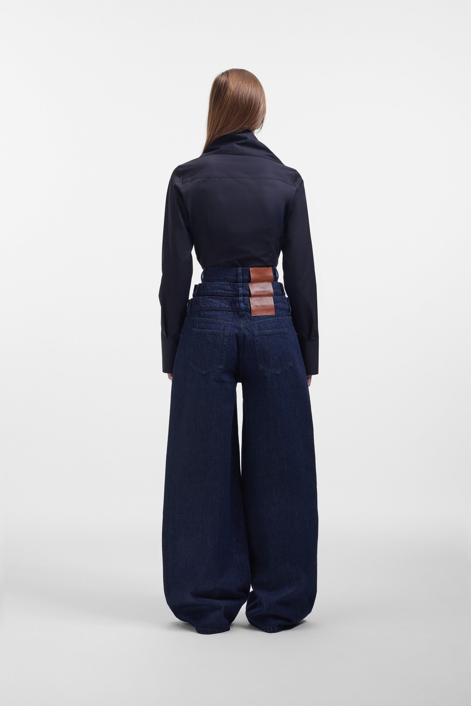 Model wearing a black long sleeve shirt with a bow on the collar, styled with dark denim pants on a white background.