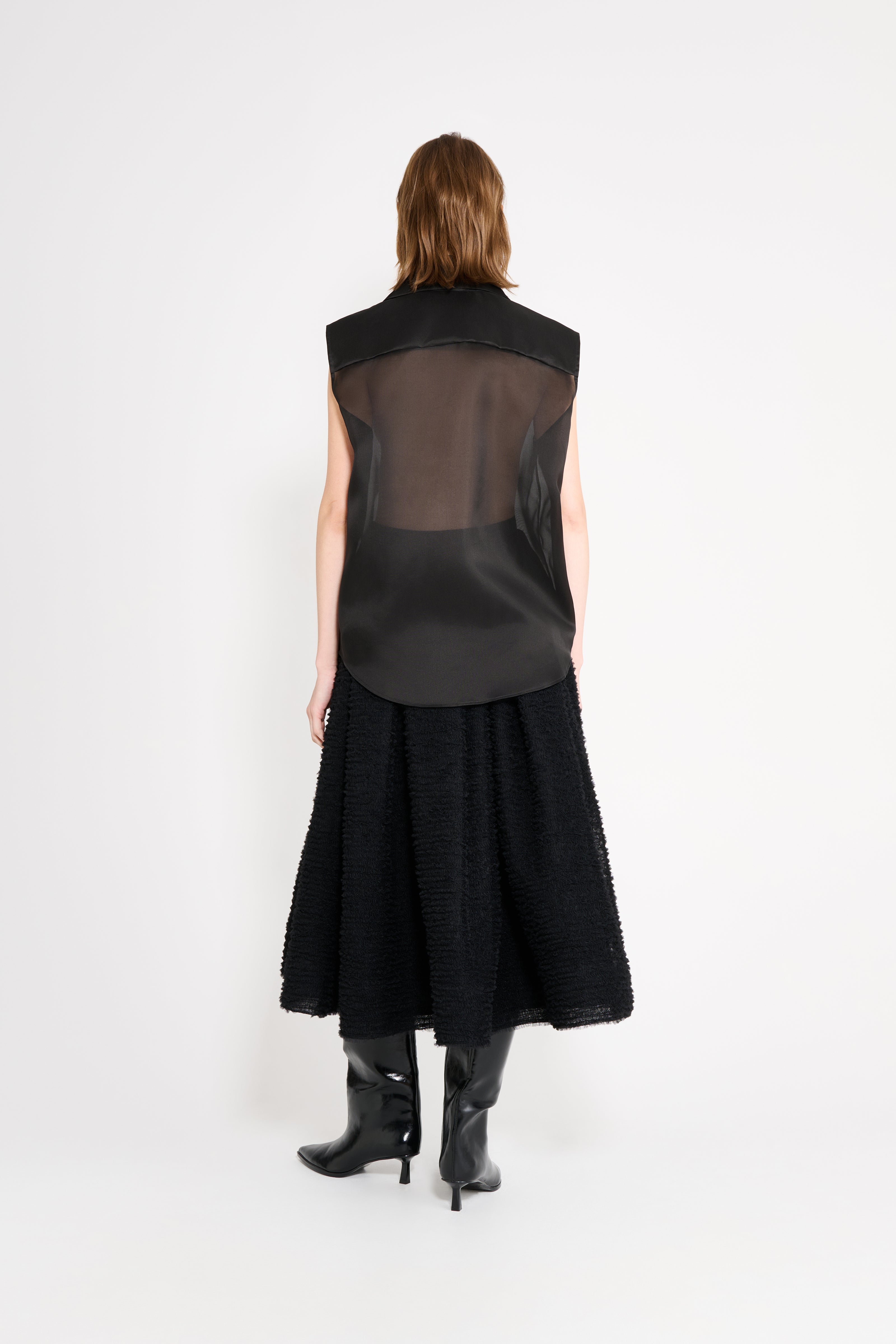 Person wearing a black sleeveless dress with sheer overlay on a white background