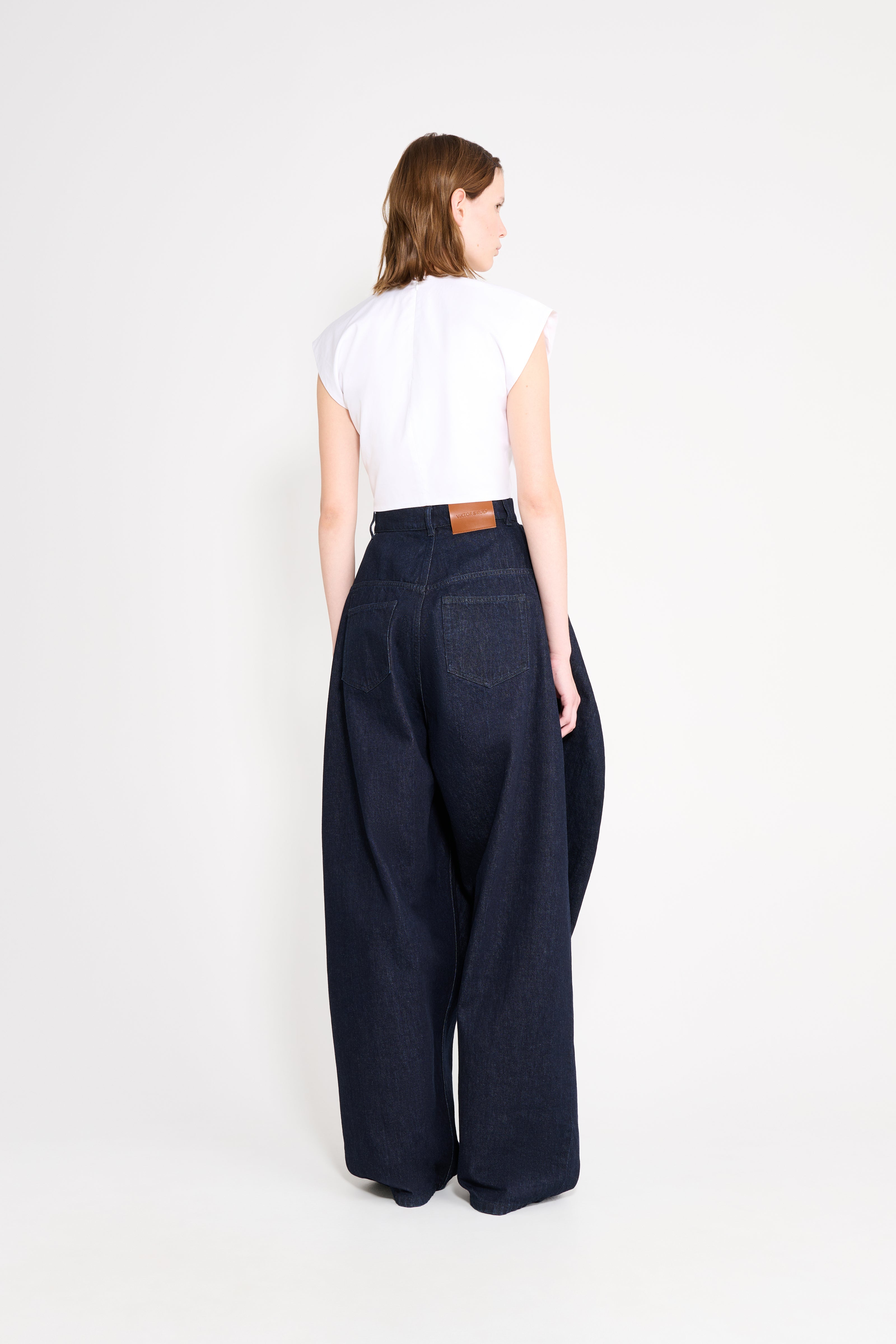 Person wearing dark blue wide-leg pants and a white top on a white background