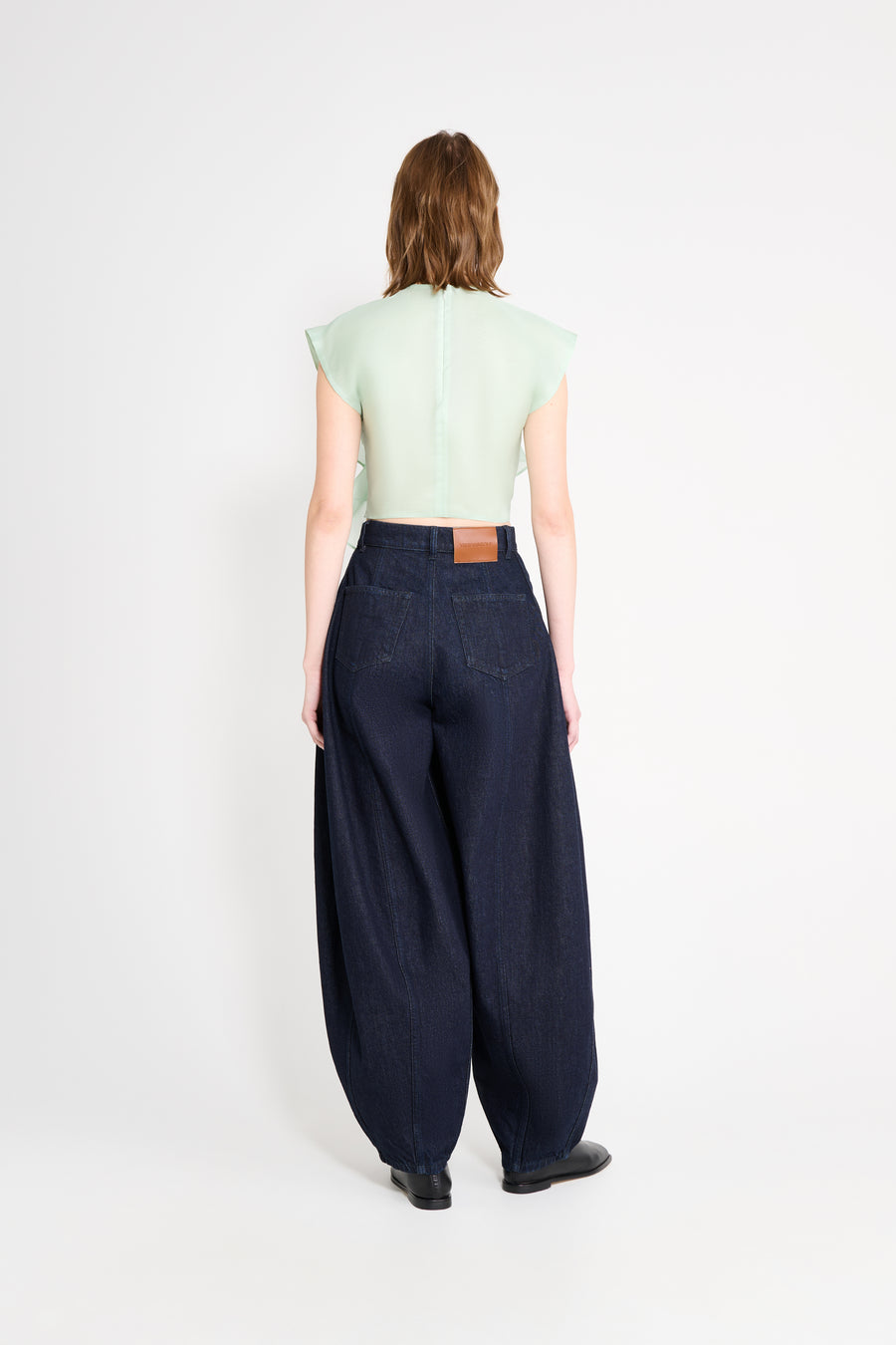 Person wearing a light green crop top and dark blue wide-leg pants on a white background