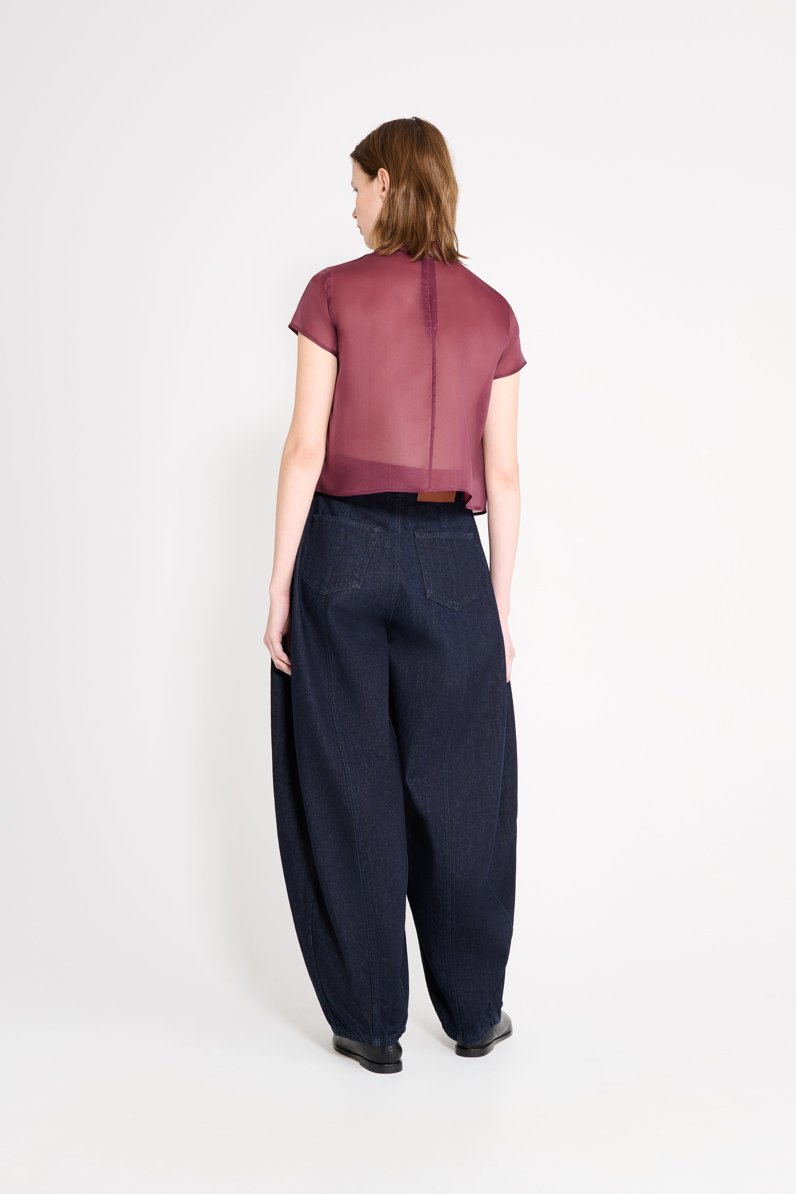 Woman wearing a maroon top and dark blue pants on a white background