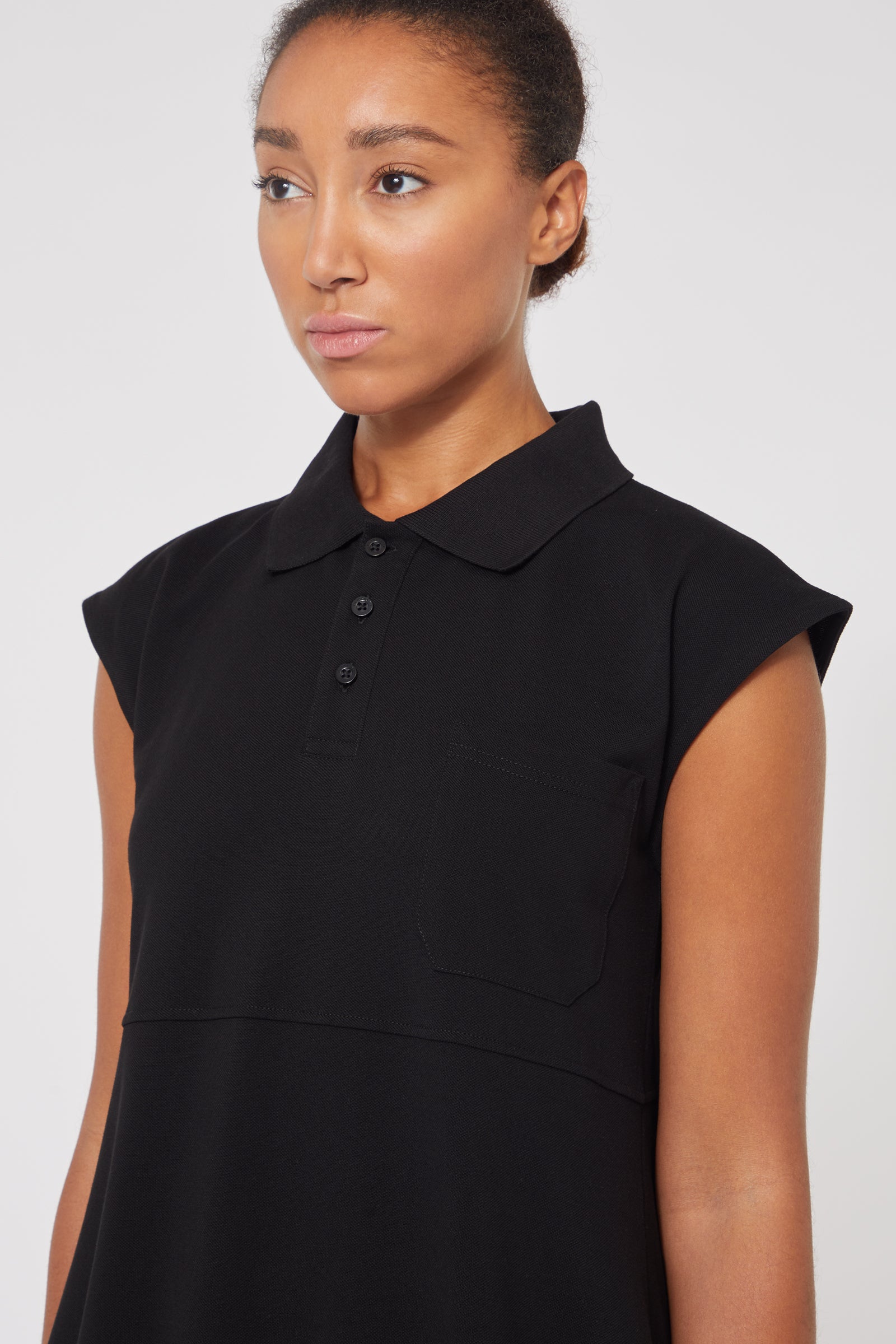 Black sleeveless polo shirt featuring a classic collar and button placket, elegantly tailored with a front pocket design.