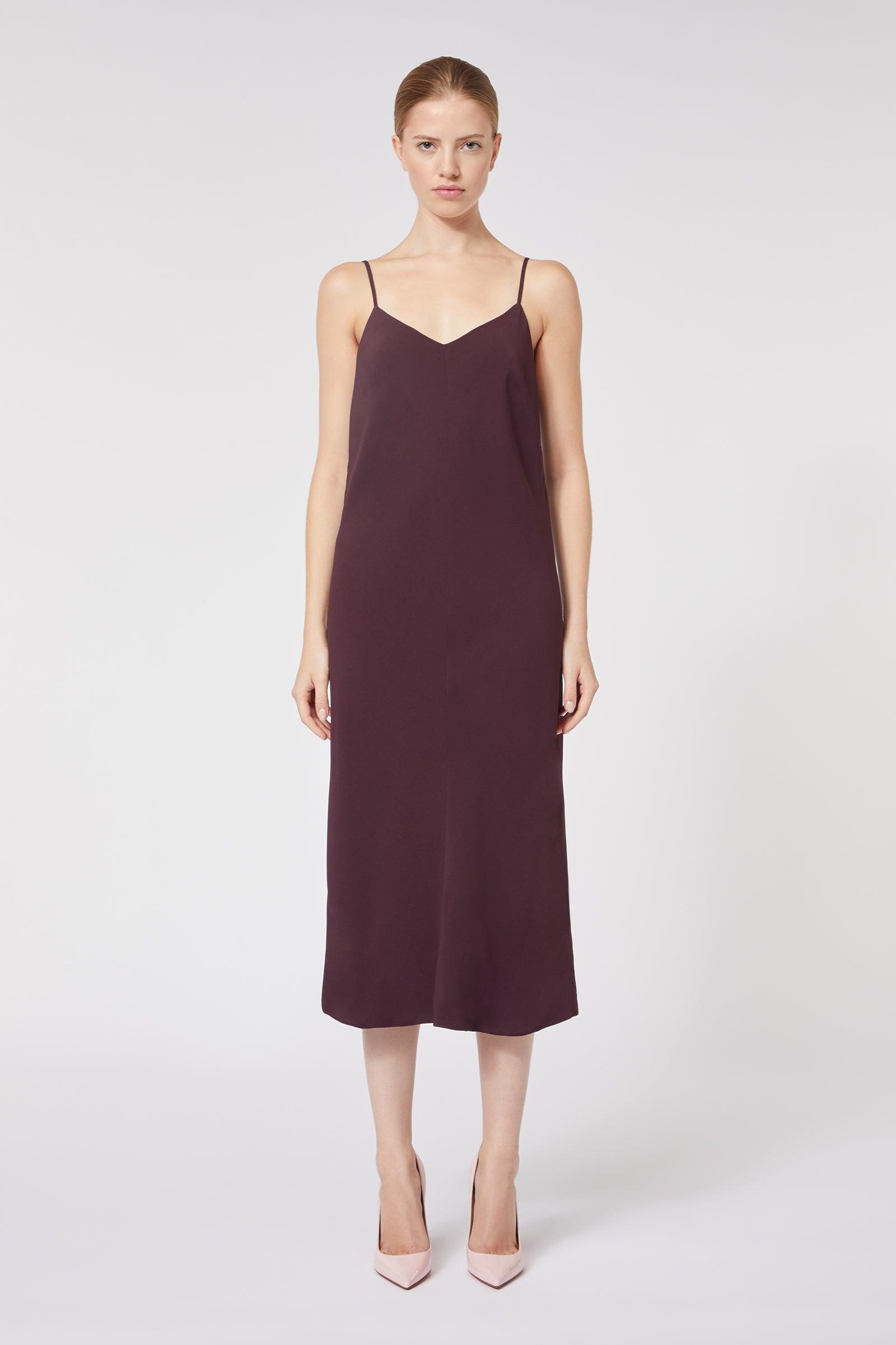 A model wears a sleeveless dark burgundy midi dress with spaghetti straps, paired with elegant pale pink pointed heels.