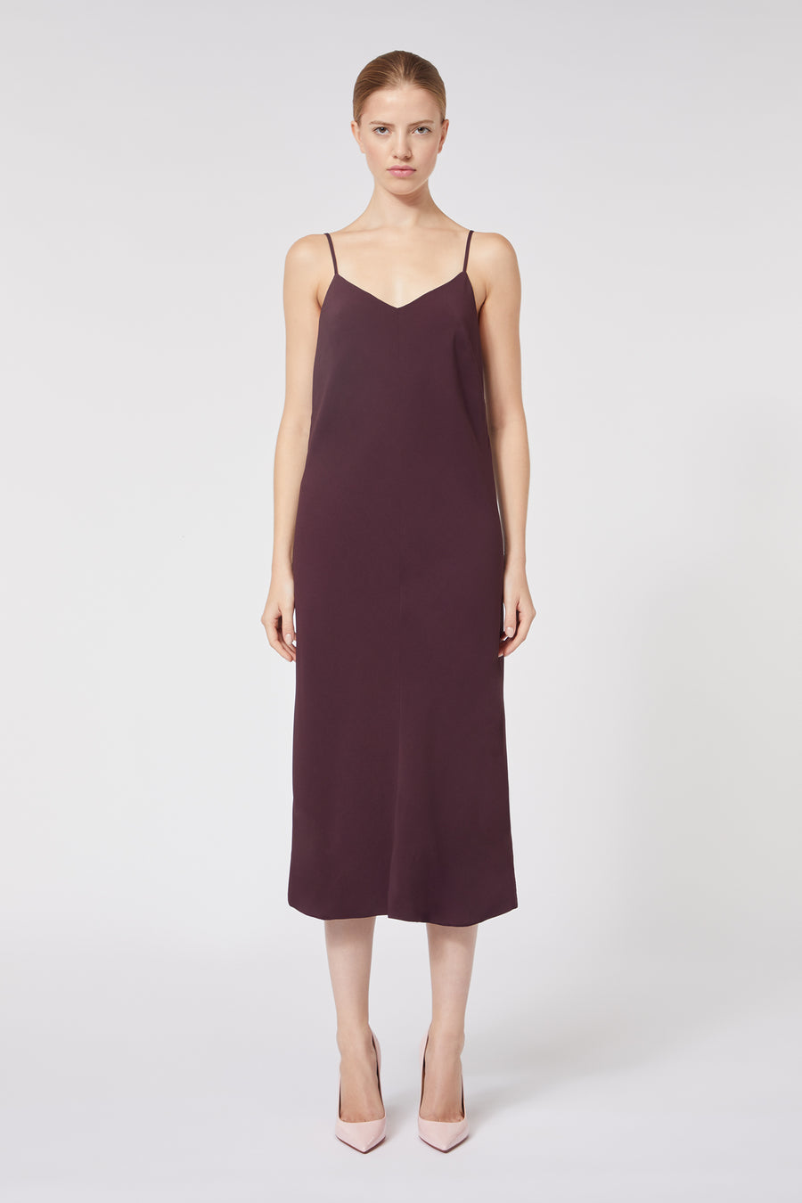 A model wears a sleeveless dark burgundy midi dress with spaghetti straps, paired with elegant pale pink pointed heels.