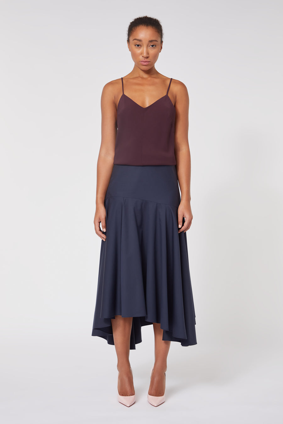 Elegant camisole in deep plum with thin straps paired with a flowing navy high-low midi skirt and blush heels.