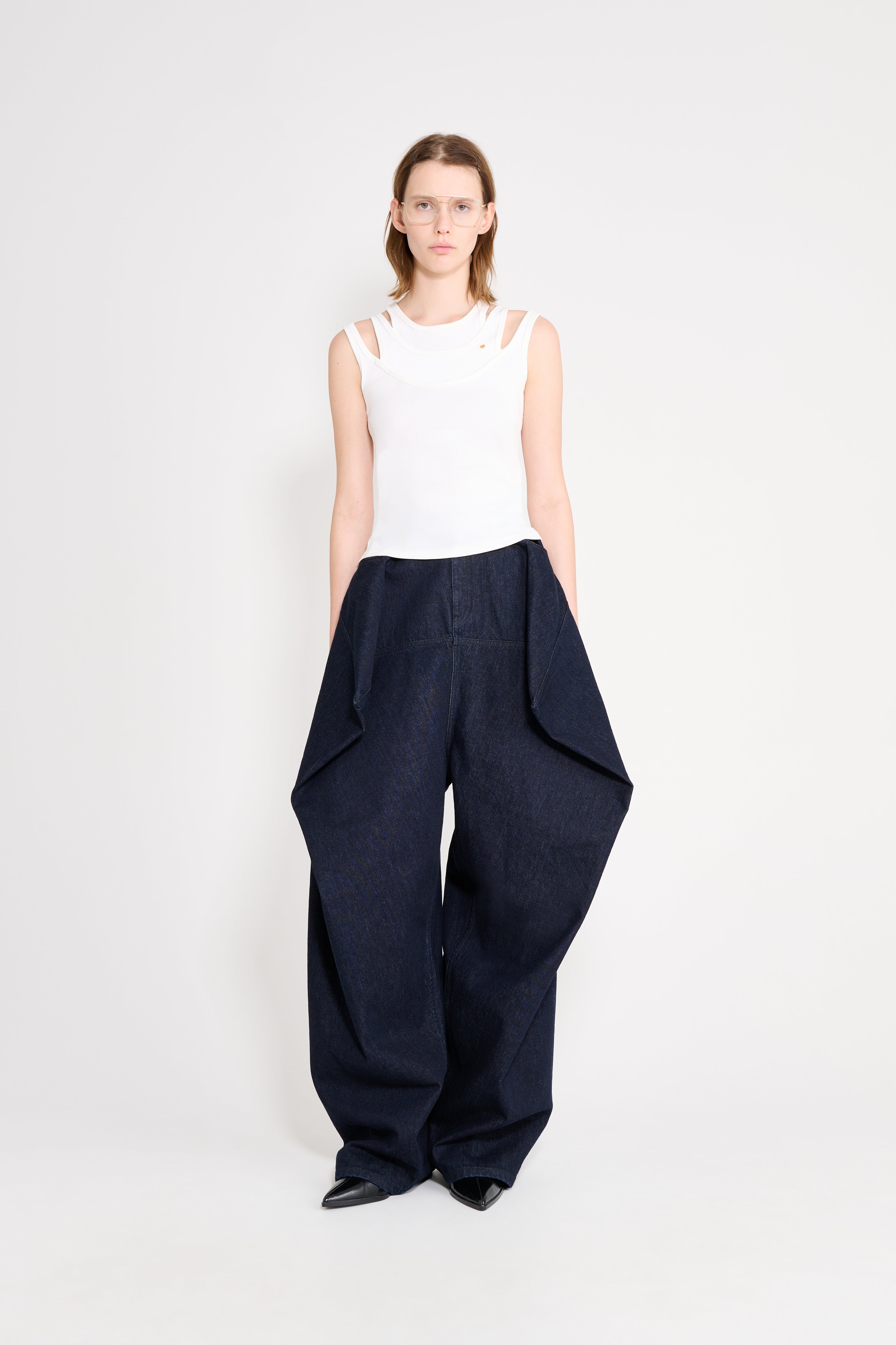 Woman wearing a white sleeveless top and navy wide-leg pants on a white background