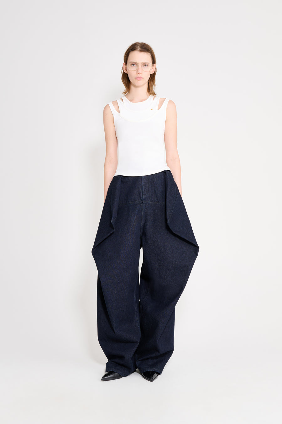 Woman wearing a white sleeveless top and navy wide-leg pants on a white background